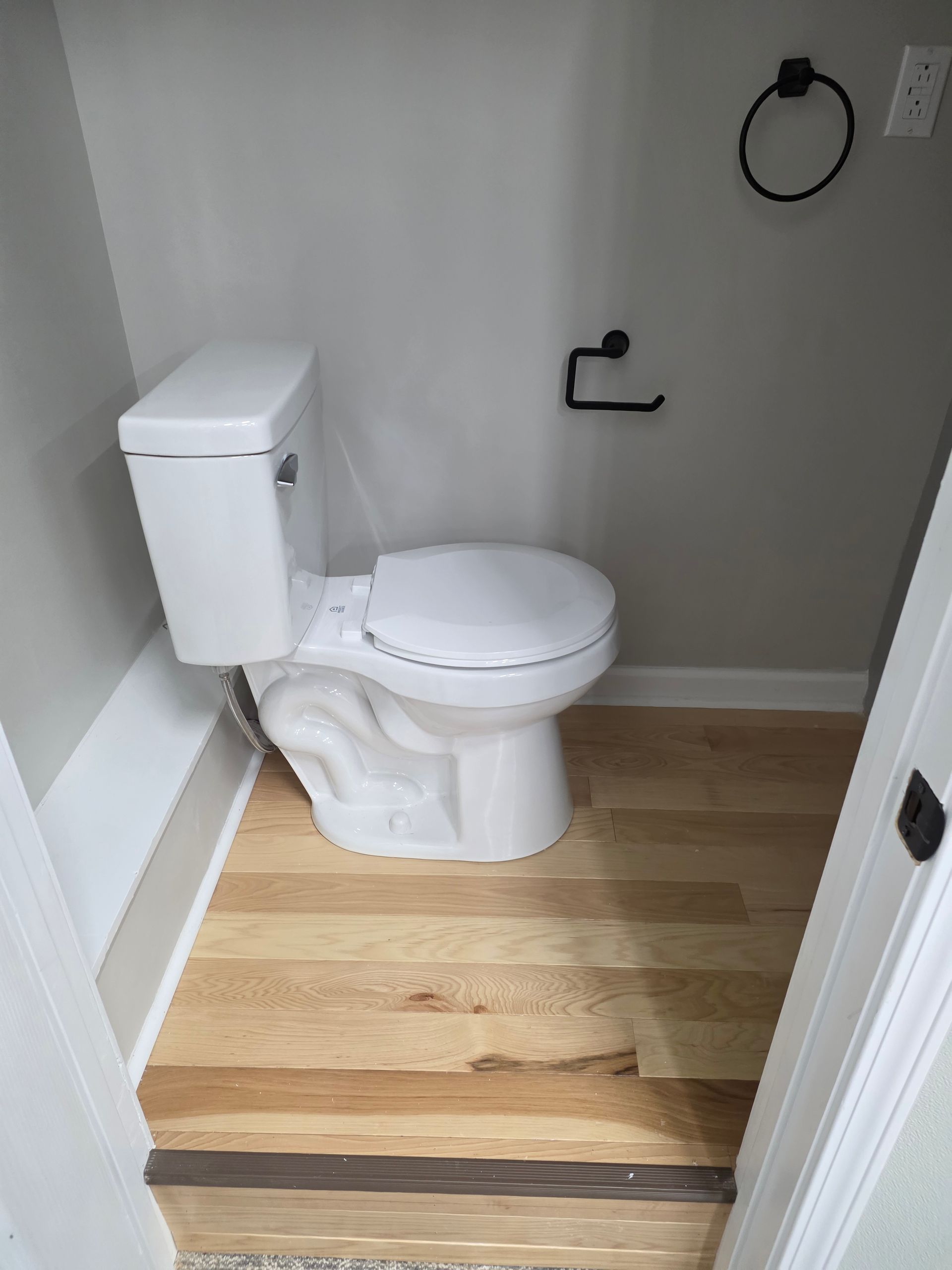 Small bathroom with a white toilet, gray walls, and light wood flooring.