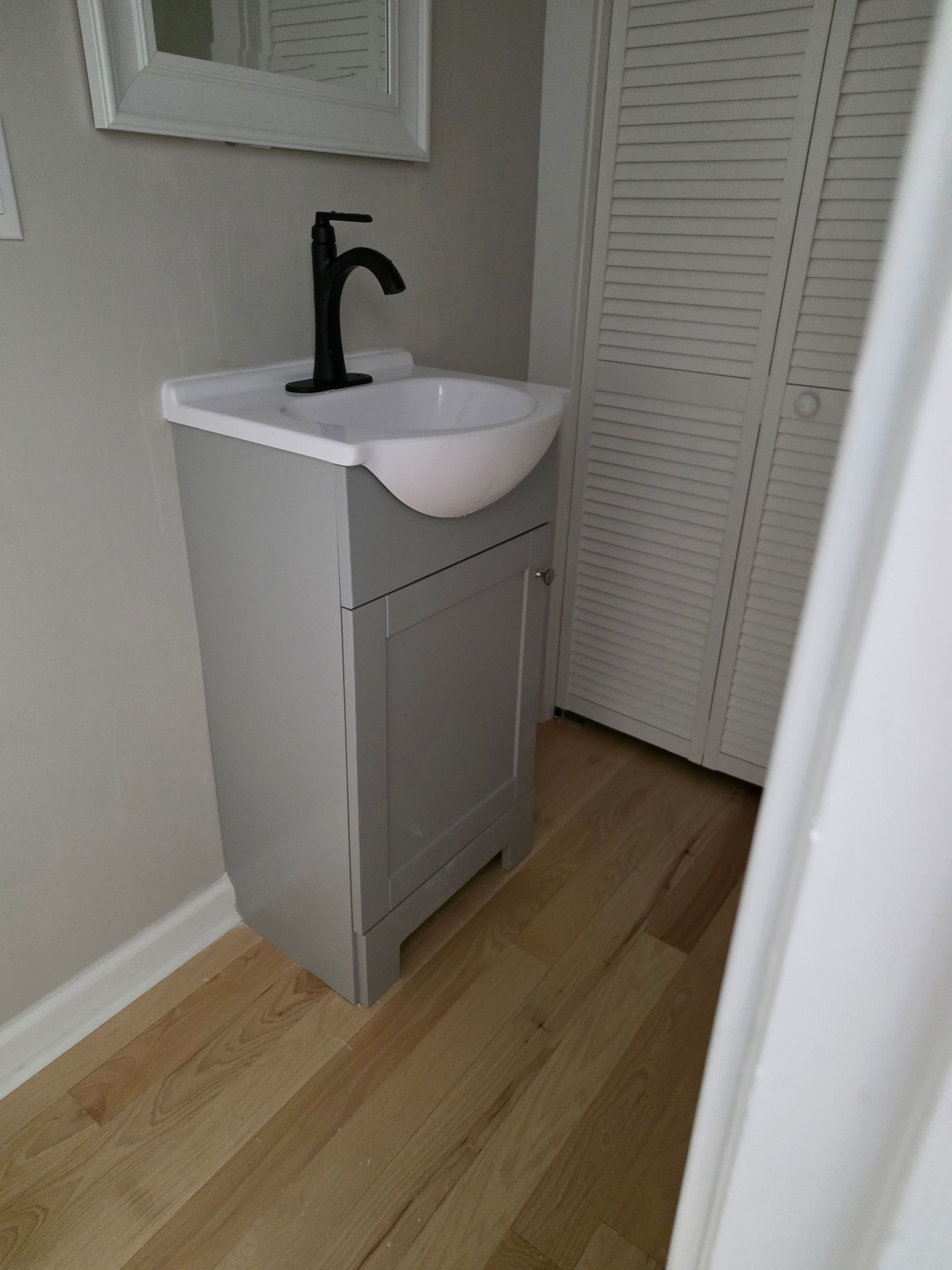 Small white bathroom vanity with a black faucet in a narrow hallway.