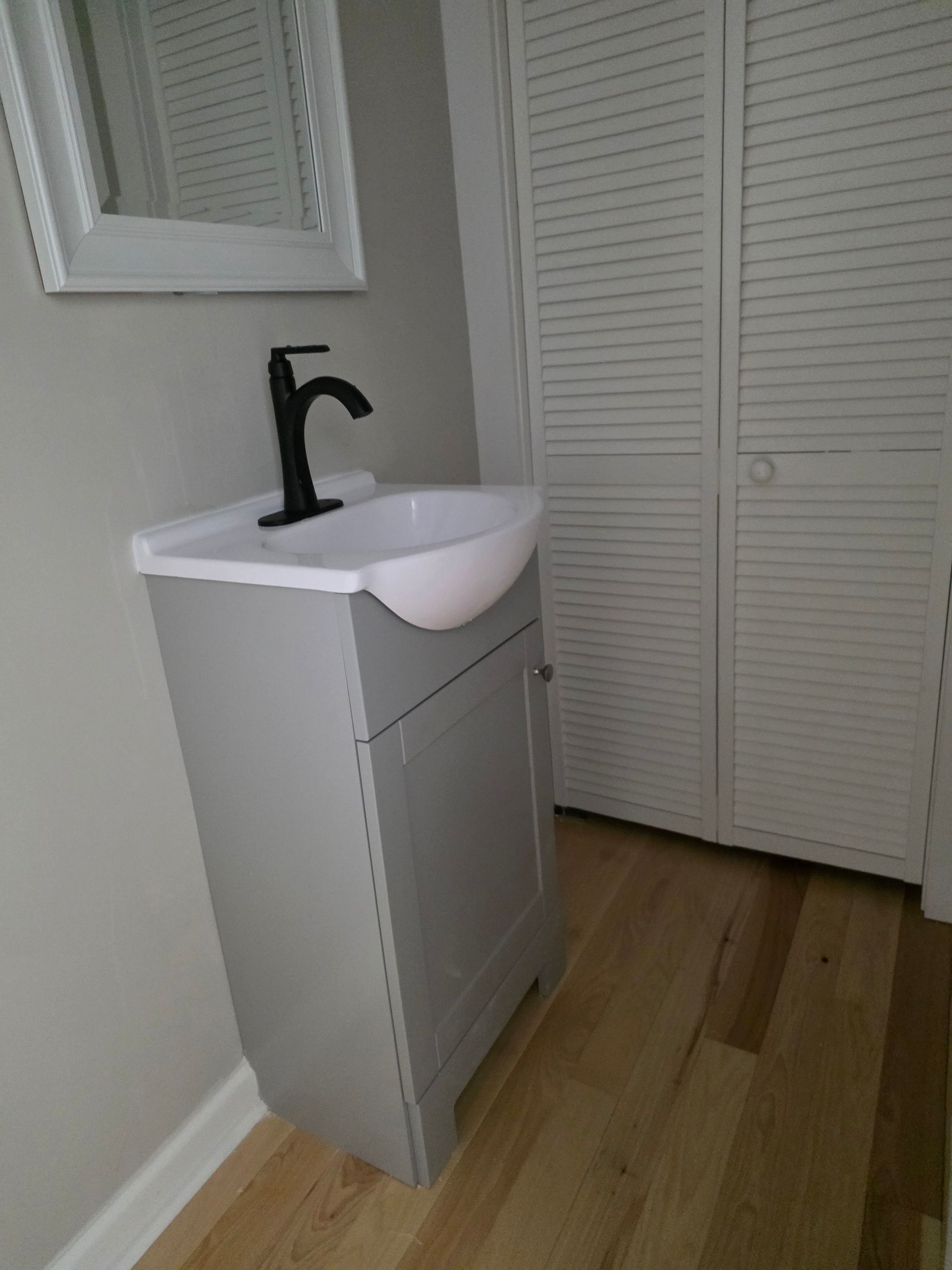 Small white bathroom vanity with black faucet and sink beside louvered closet doors.