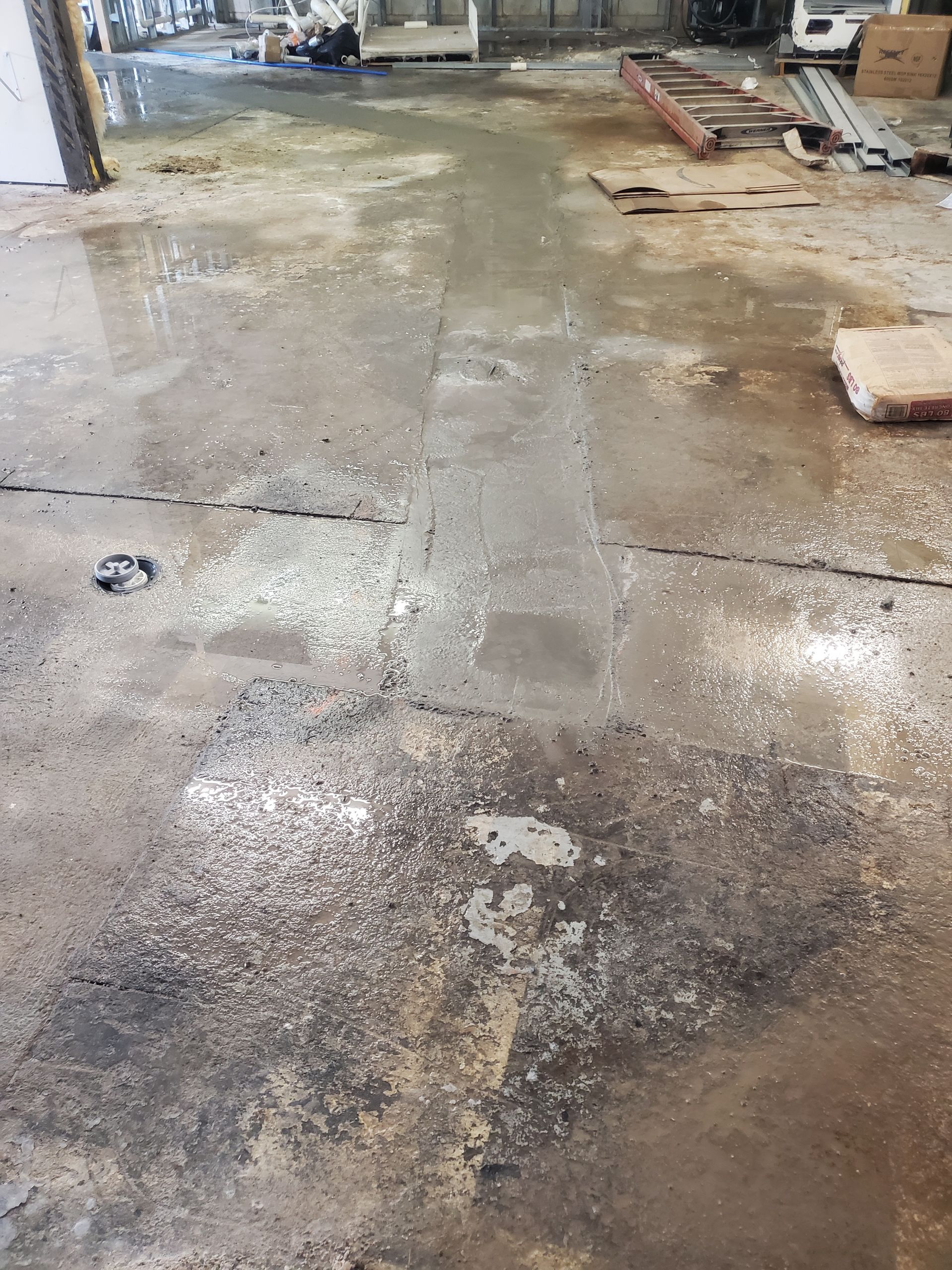 Wet, muddy construction floor with puddles and scattered debris