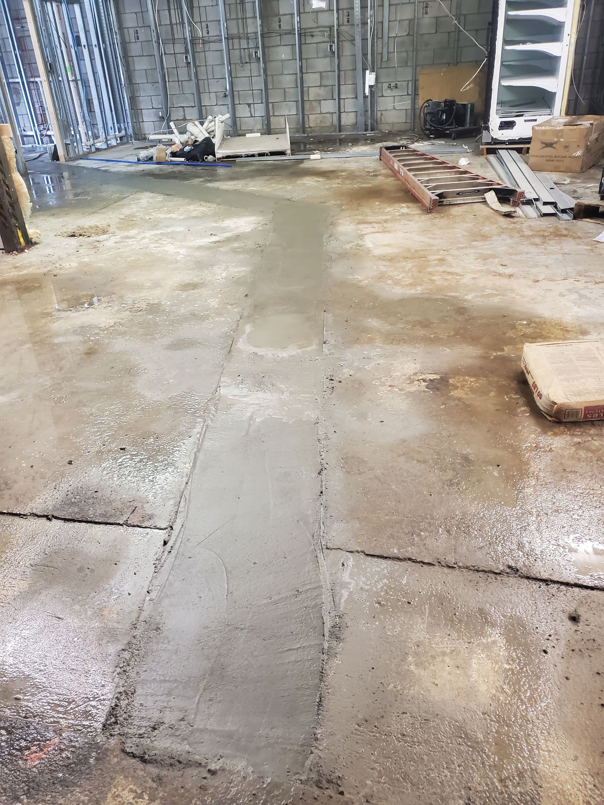 Wet concrete floor in an unfinished warehouse with construction materials scattered around