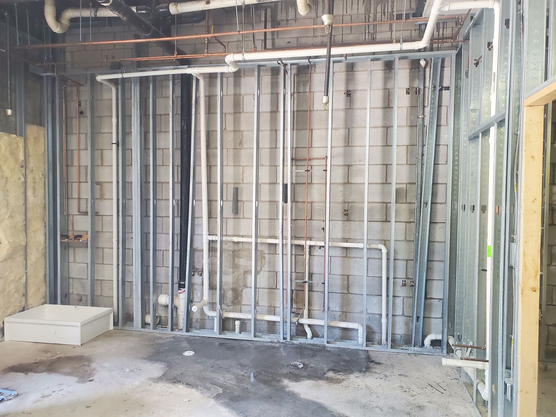 Exposed interior wall framing and plumbing in an unfinished room with concrete floor.