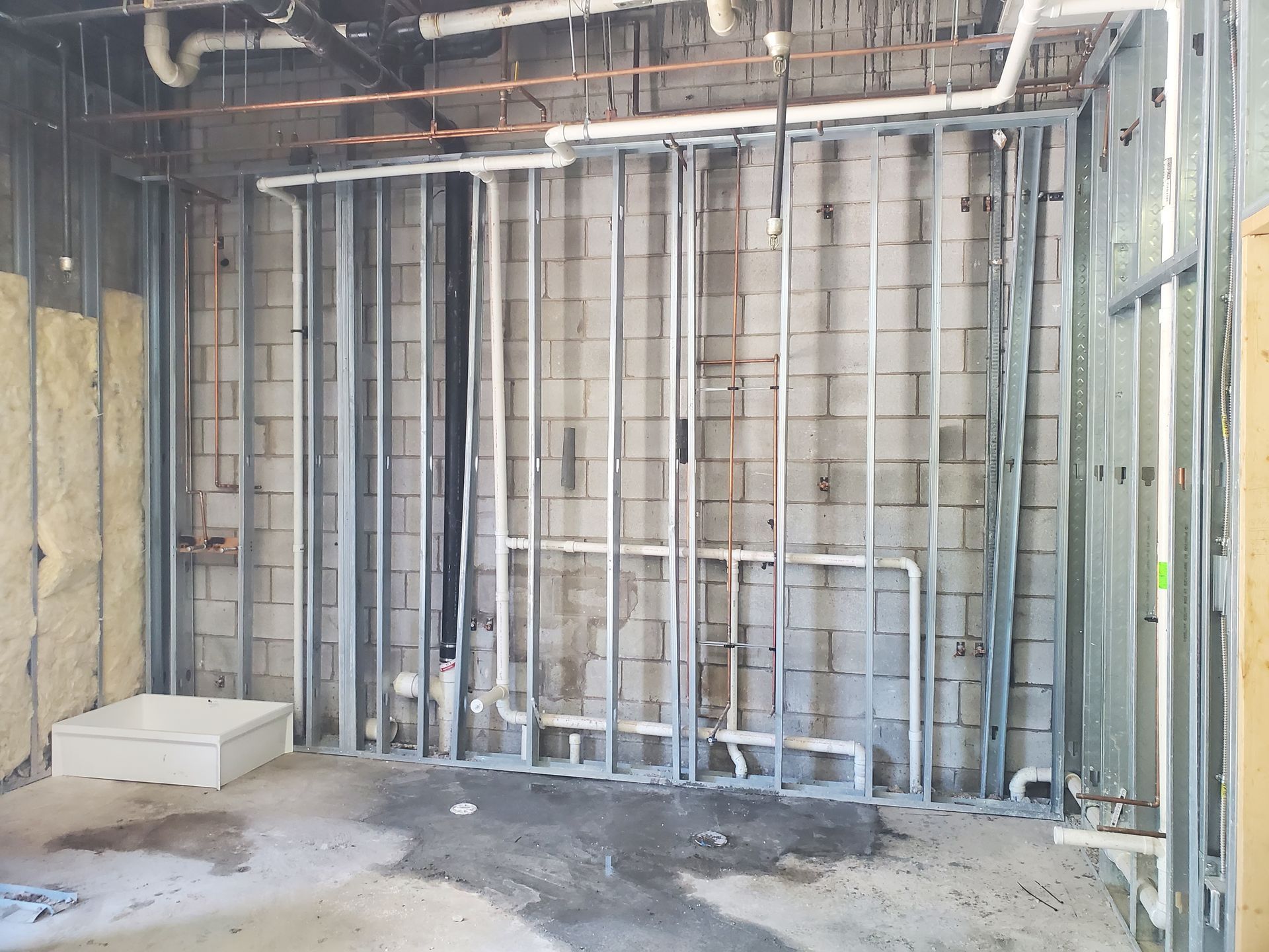 Empty construction room with exposed wall studs, insulation, and concrete floor