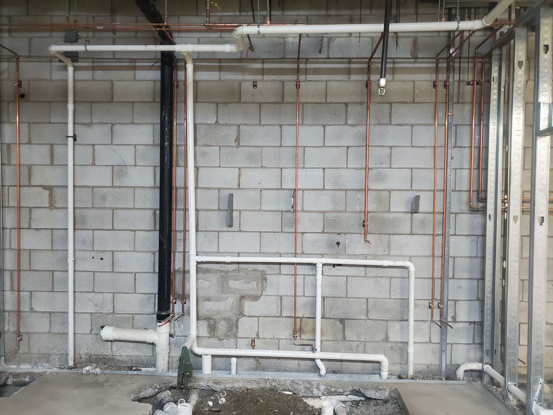 Exposed cinder block wall with white and black plumbing pipes in an unfinished basement or utility room
