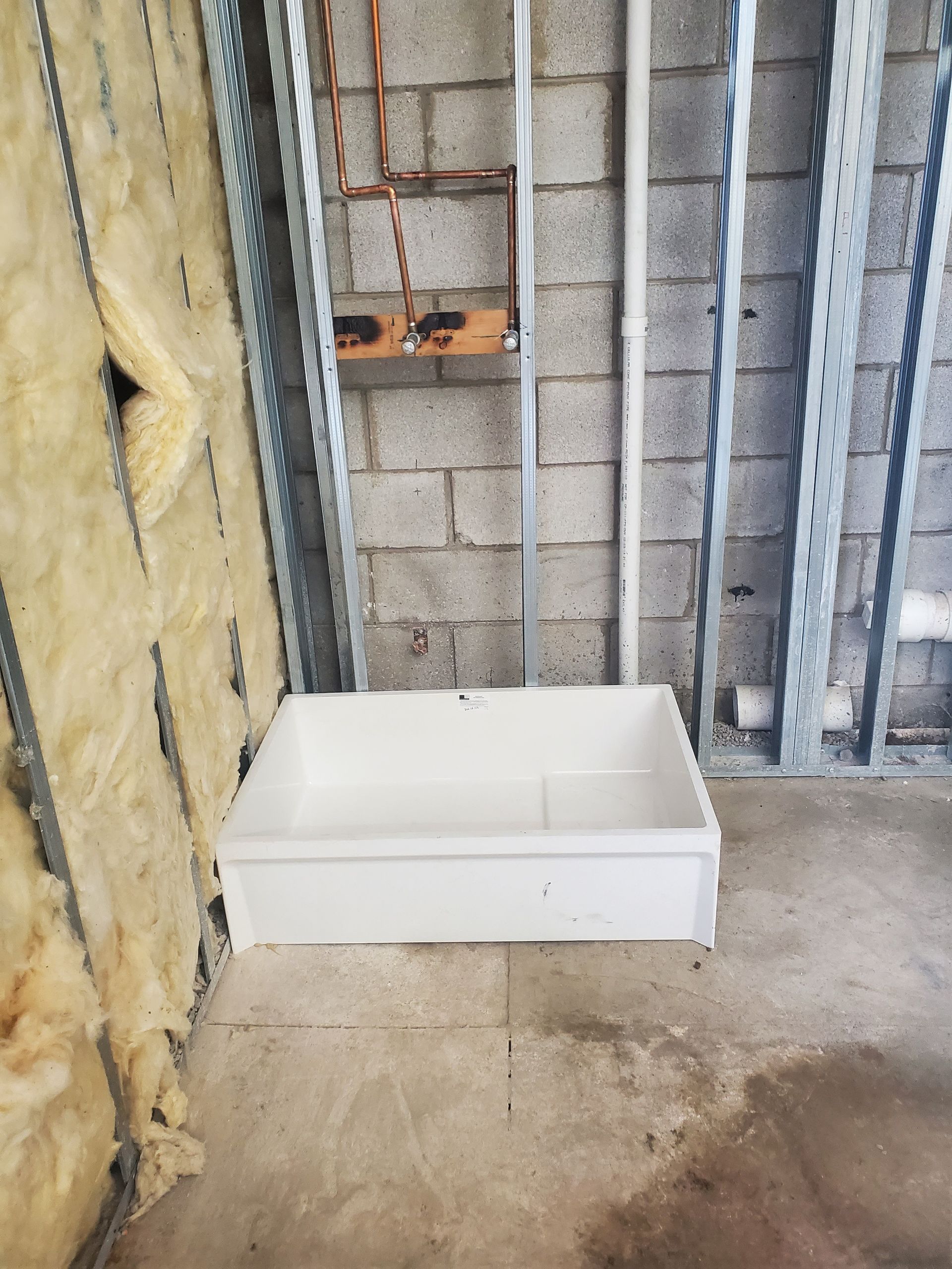 White rectangular box on a concrete floor beside exposed wall insulation and metal studs in an unfinished room