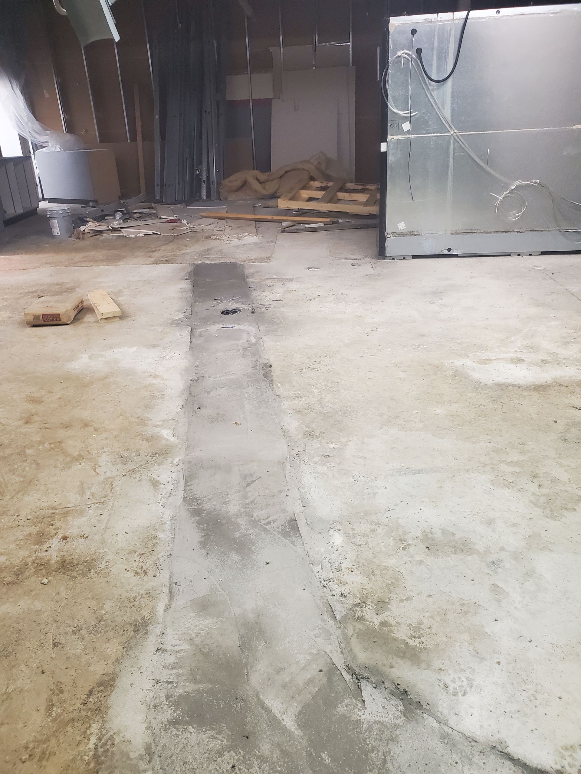 Abandoned warehouse interior with concrete floor, debris, and stacked materials near the back wall