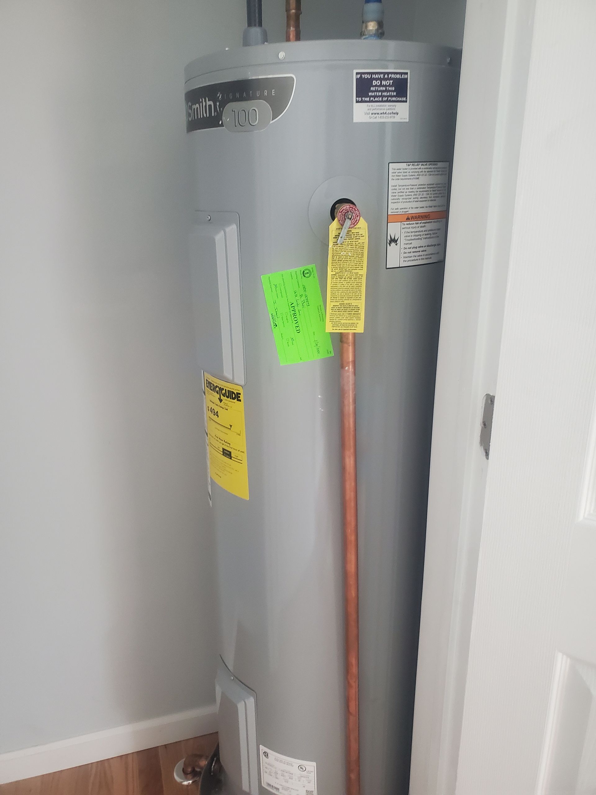 Gray water heater with colored inspection tags in a utility closet