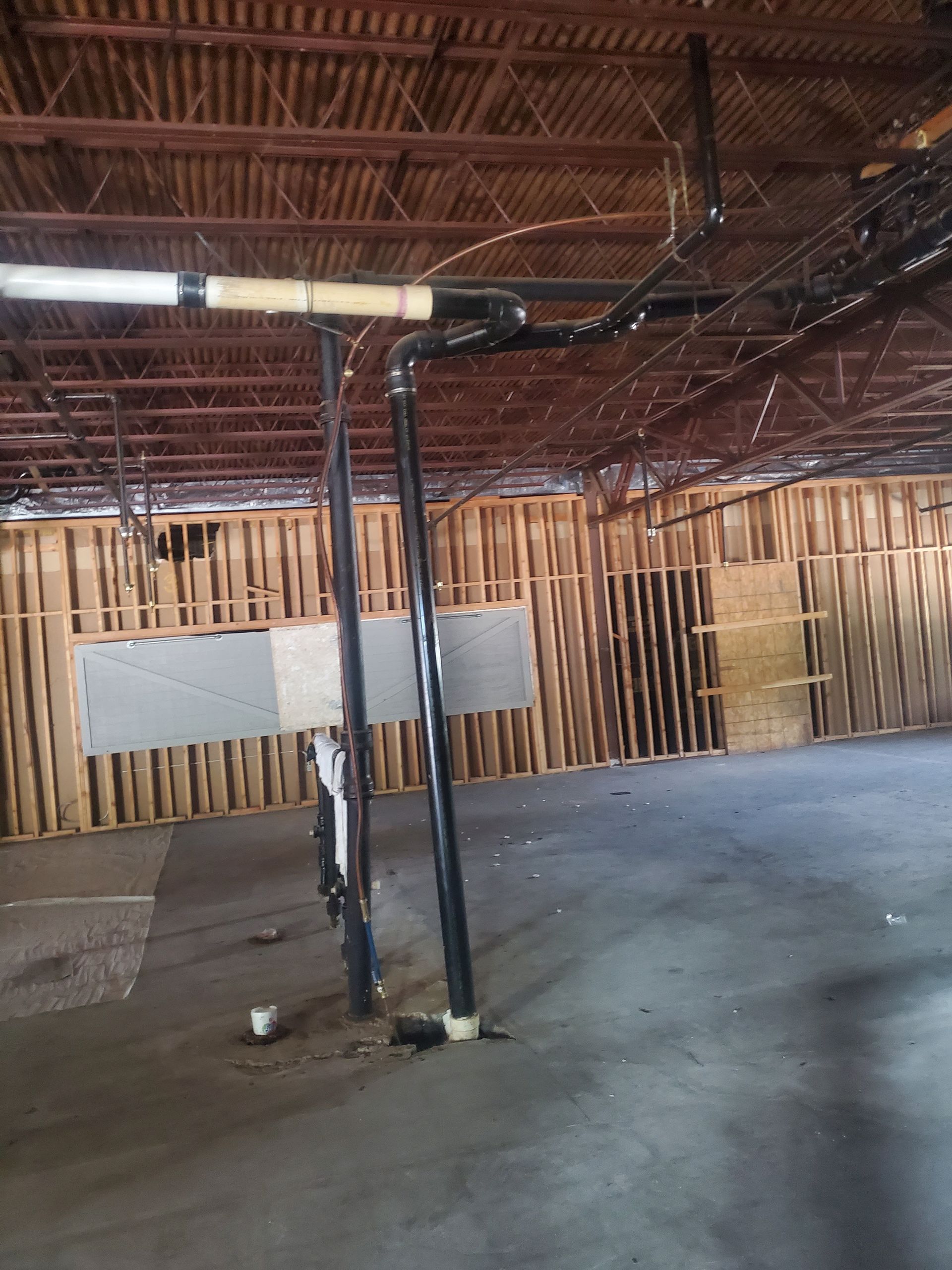 Empty warehouse interior with exposed beams, wooden wall panels, and two vertical pipes on a concrete floor
