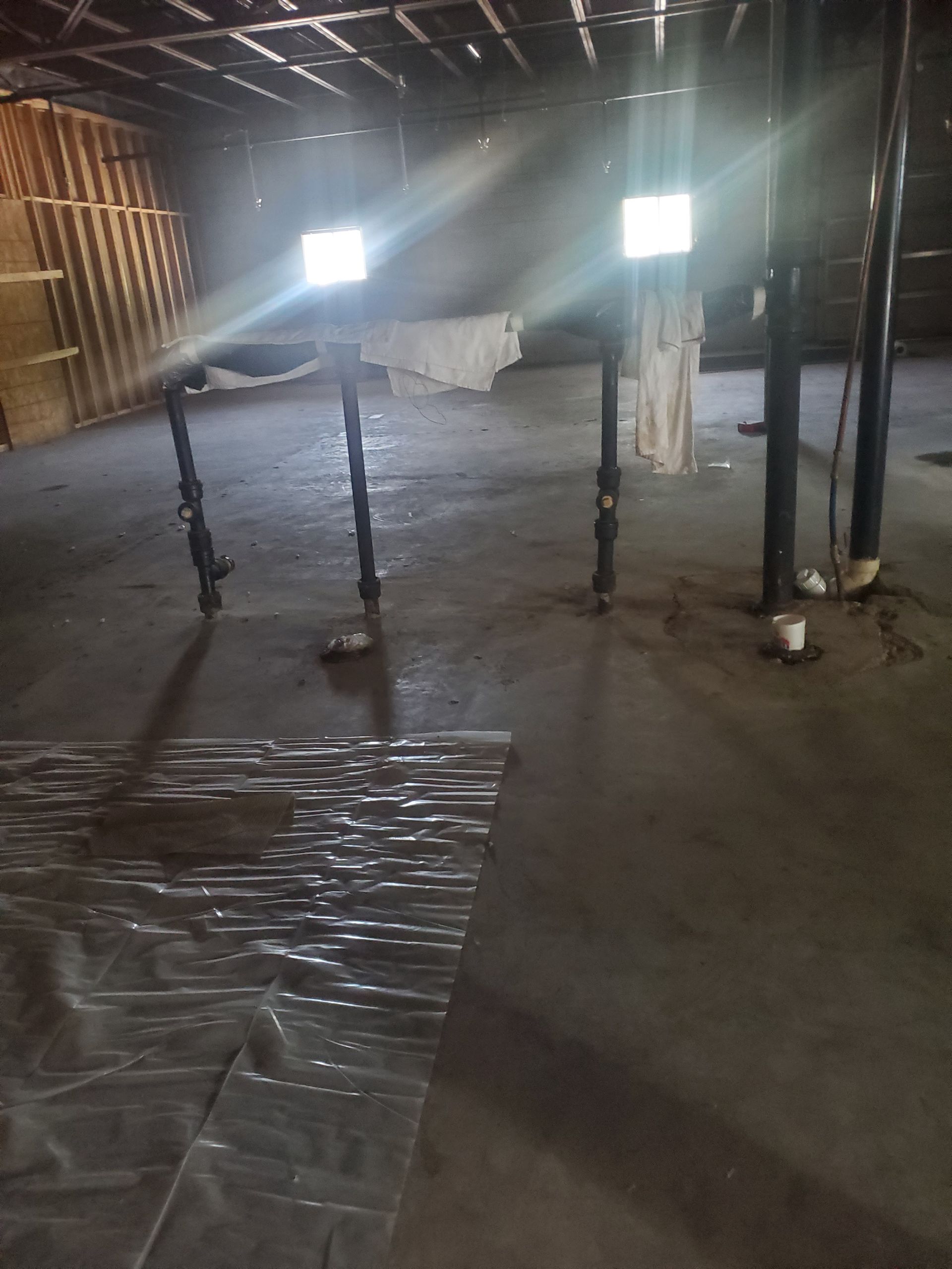 Dim attic with exposed rafters, hanging fabric, wooden posts, and sunlight through small windows.