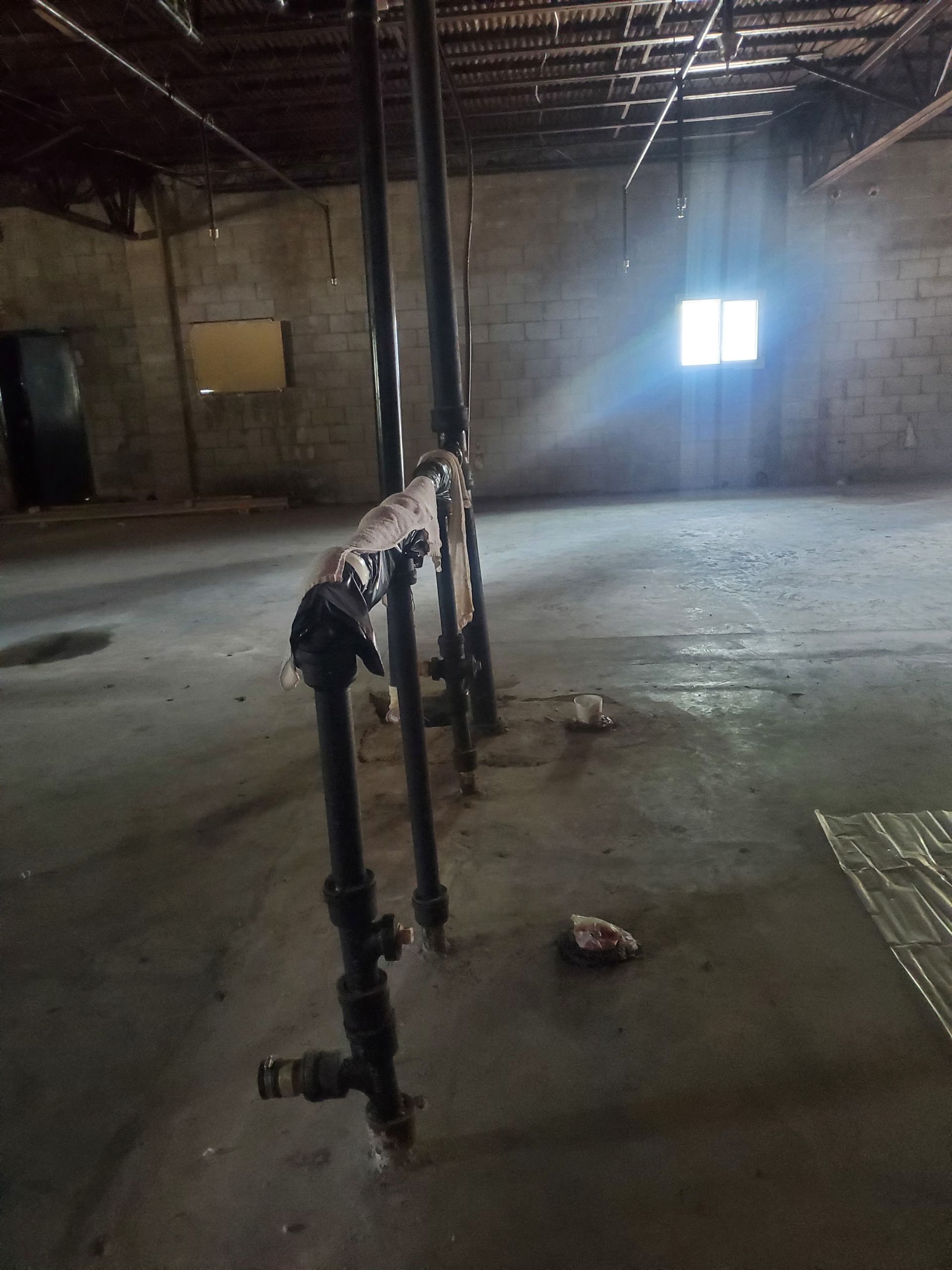 Abandoned industrial room with exposed pipes, concrete floor, and bright window light.