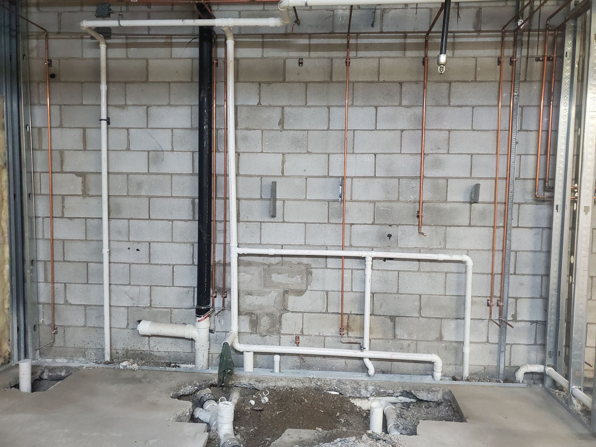 Unfinished basement with exposed pipes, cinderblock walls, and construction debris on the floor.