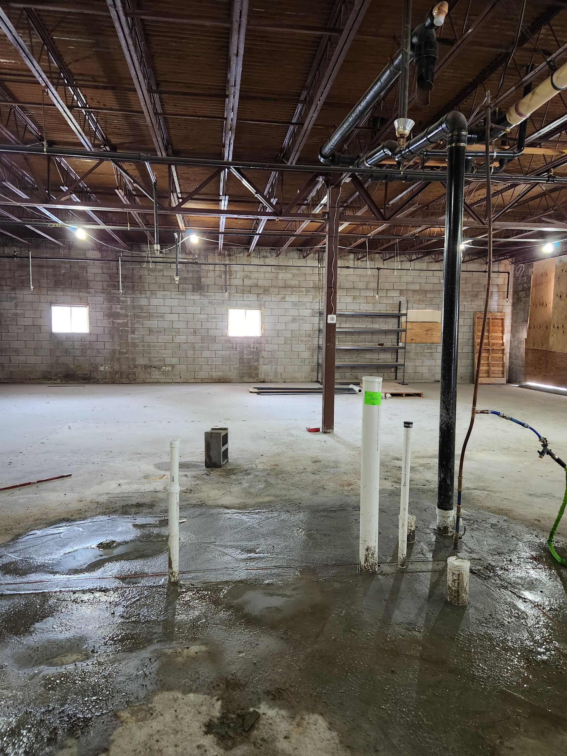 Empty industrial warehouse with wet concrete floor, exposed beams, and brick walls.