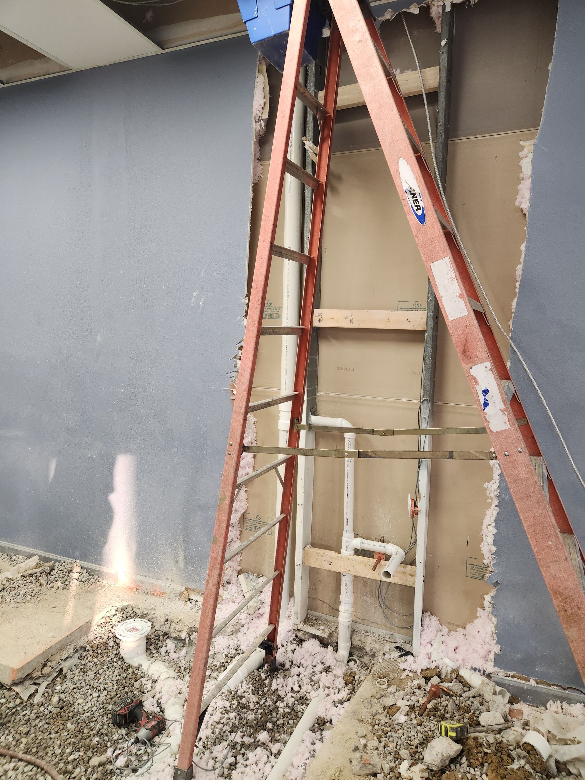 Red ladder leaning against a partially repaired exterior wall with exposed framing and debris below