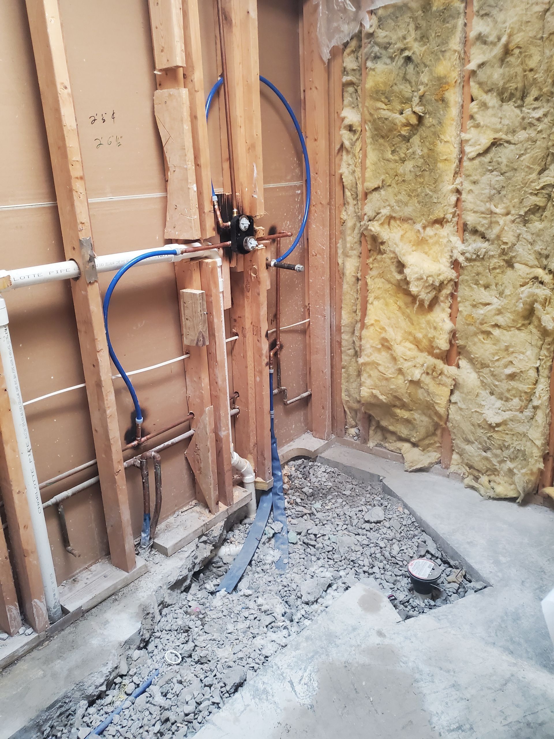 Exposed wall framing with blue wires, yellow insulation, and a rough concrete floor during renovation.