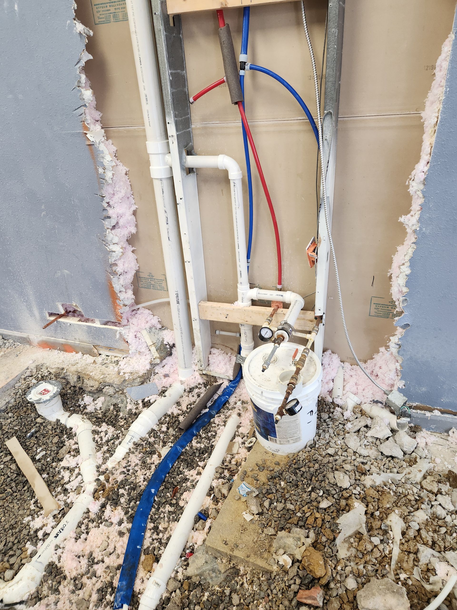 Exposed plumbing pipes in a damaged wall during construction, with debris on the floor.