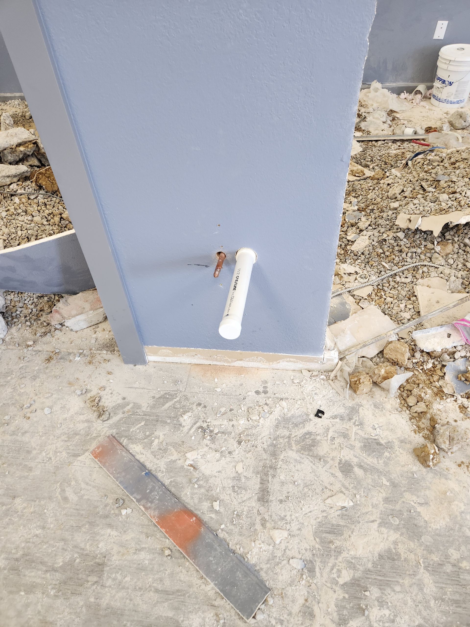 Gray utility box with a white pipe protruding near the bottom on a gravelly construction site.