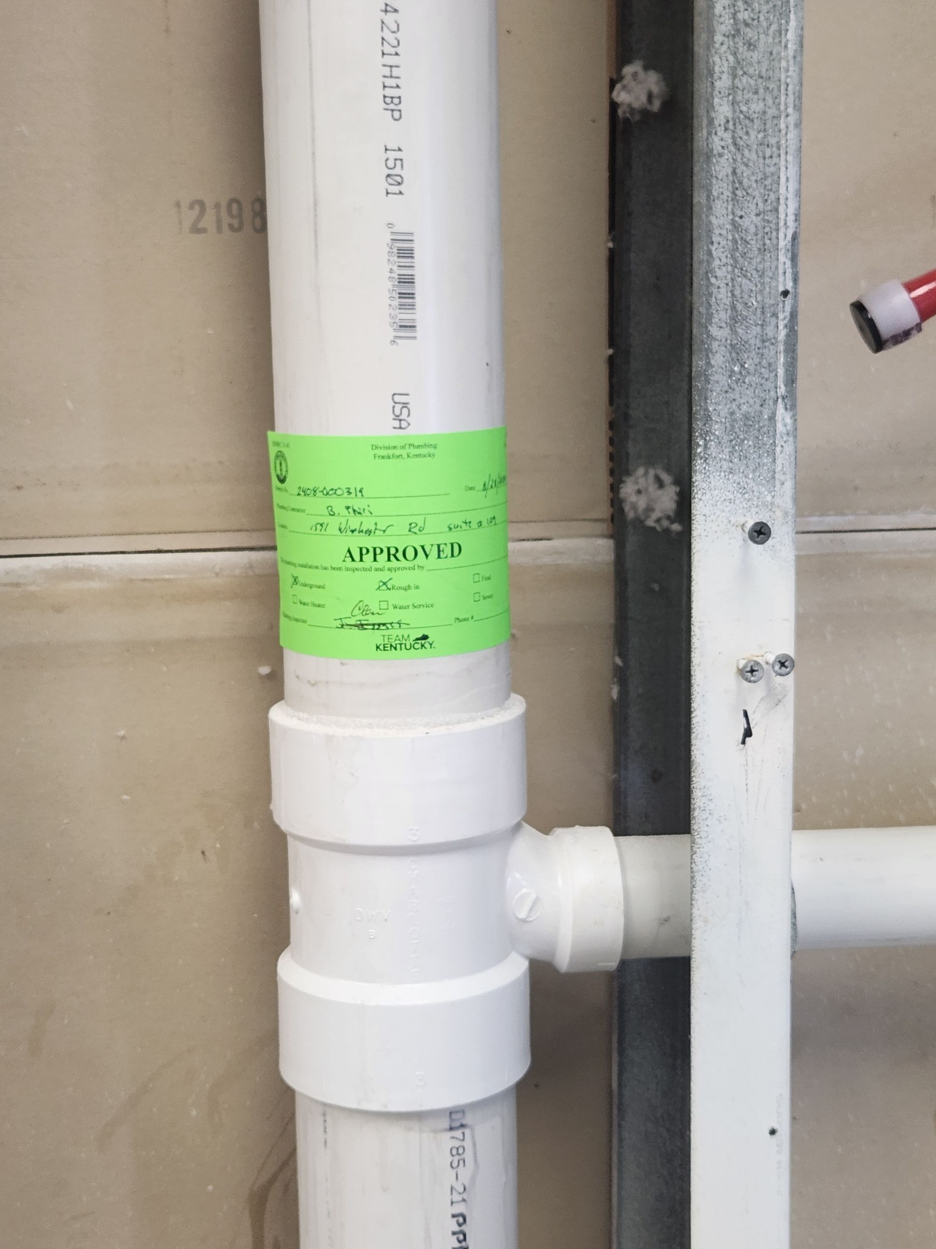 White PVC pipe with green label and side valve in an unfinished wall space