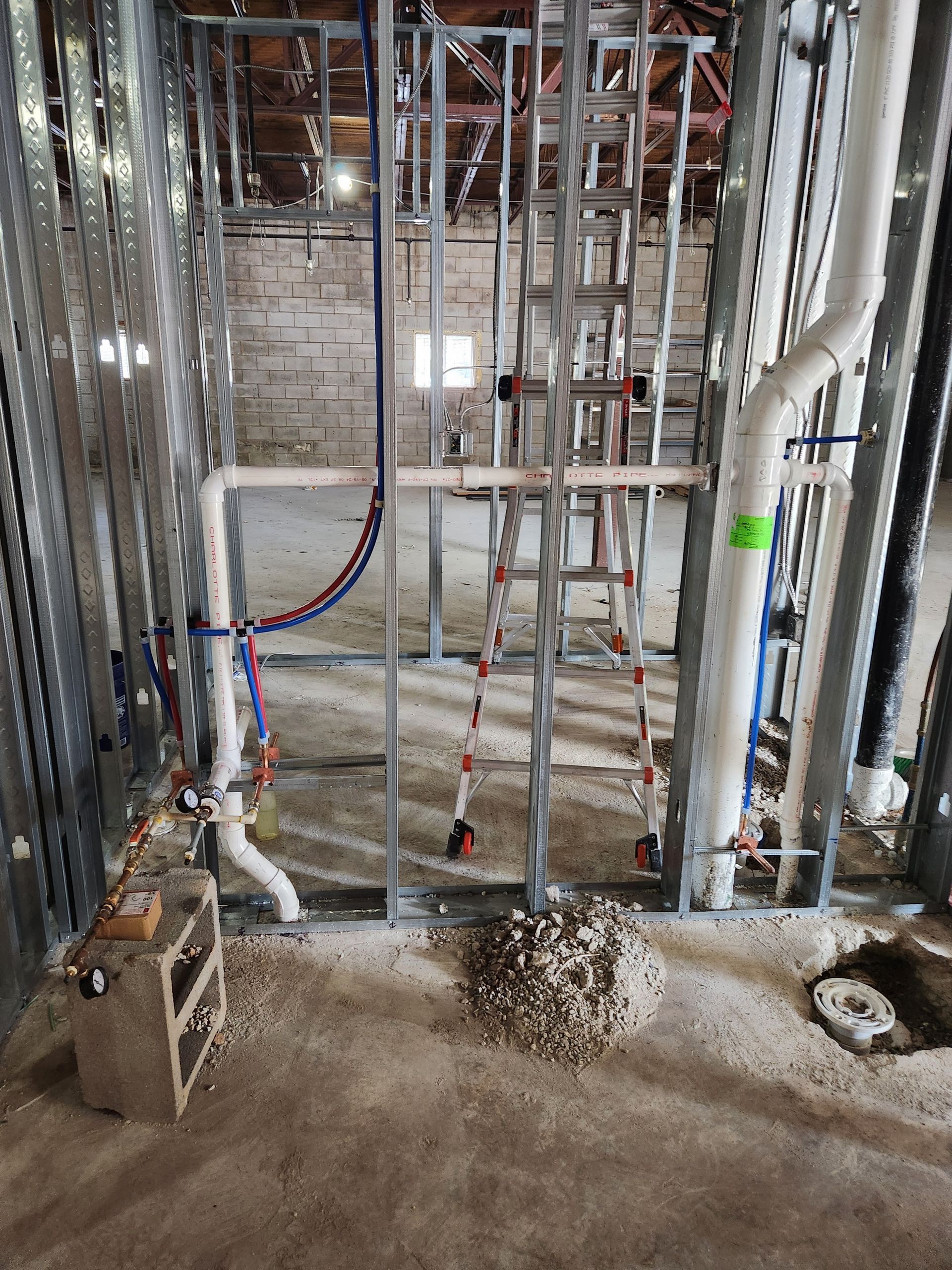 Construction site with exposed metal studs, pipes, and wiring in an unfinished wall cavity