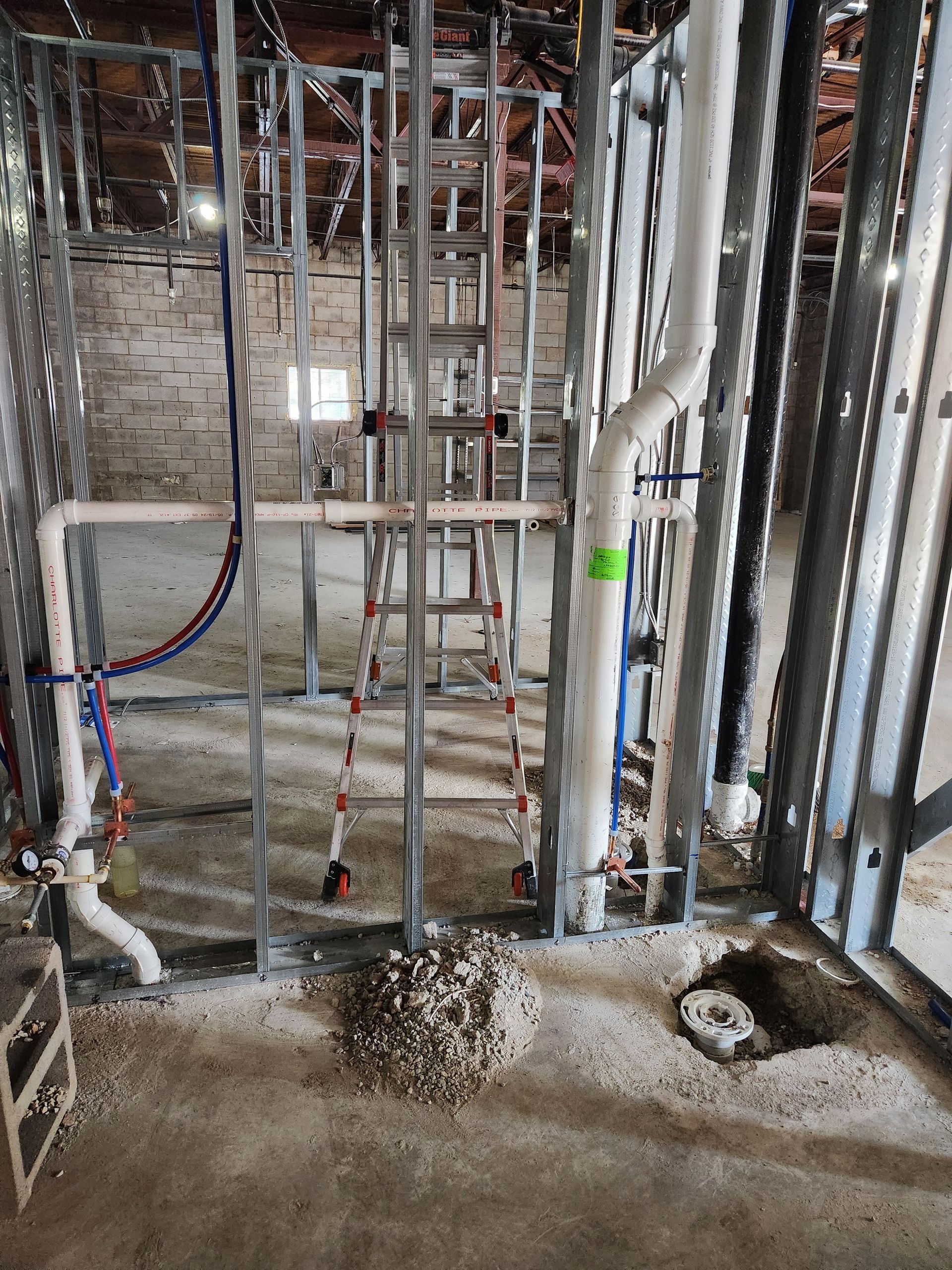 Construction site interior with exposed framing, pipes, and unfinished concrete floor.