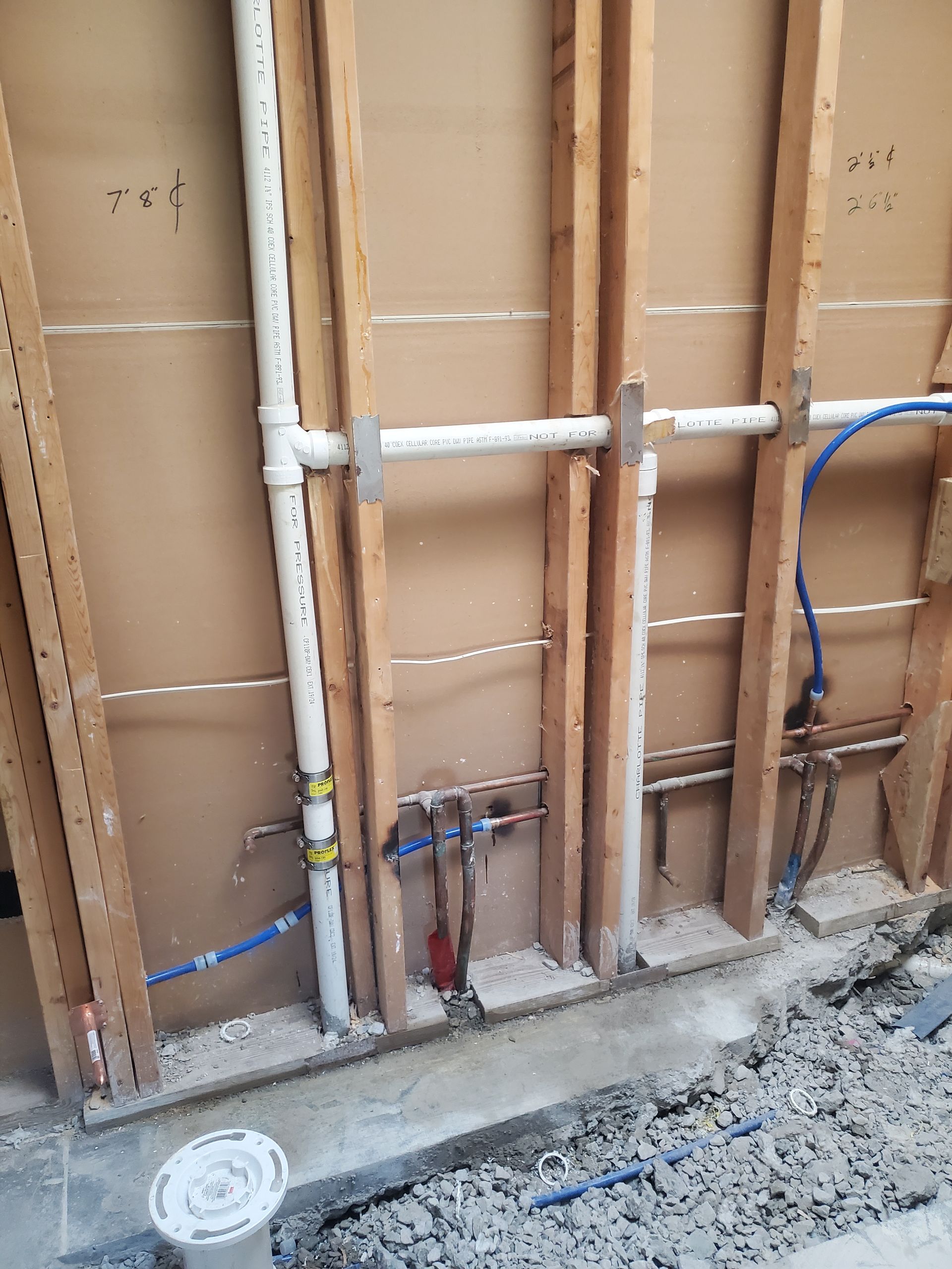 Exposed plumbing pipes and valves inside an unfinished wall with beige sheathing and gravel floor below