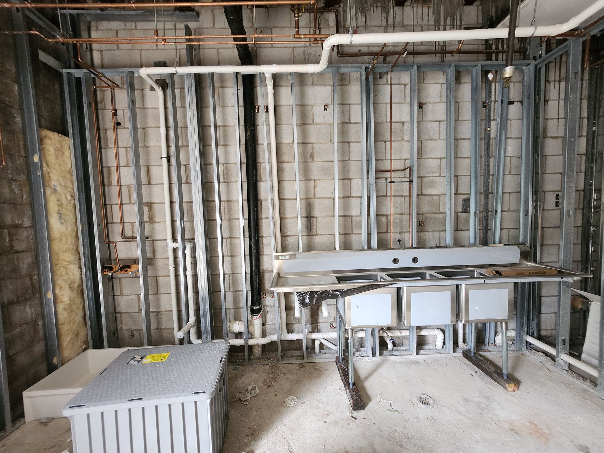 Unfinished utility room with exposed framing, pipes, and a small stainless steel sink counter.