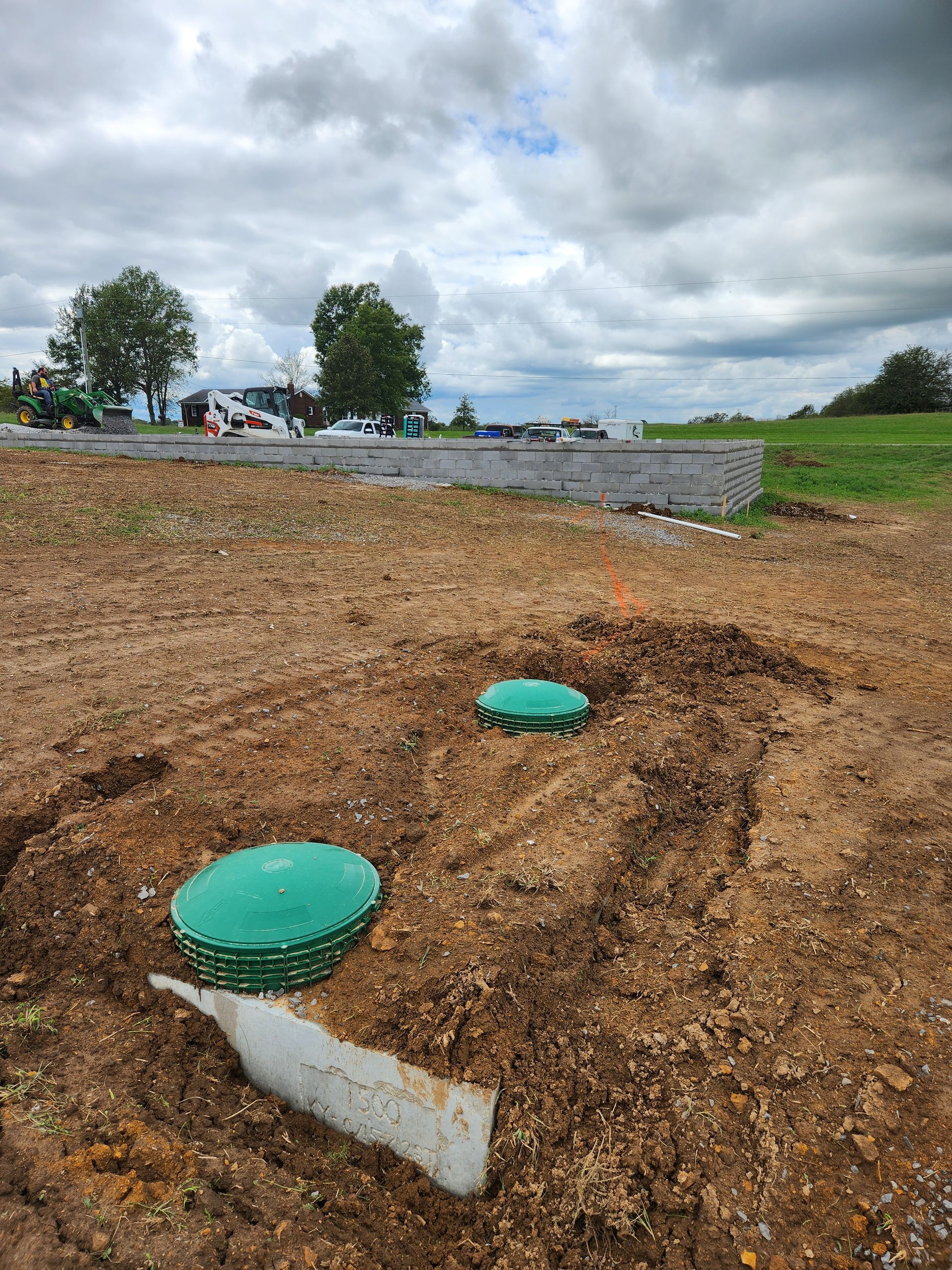 Green utility covers on a dirt slope under cloudy sky near a road and grassy field.