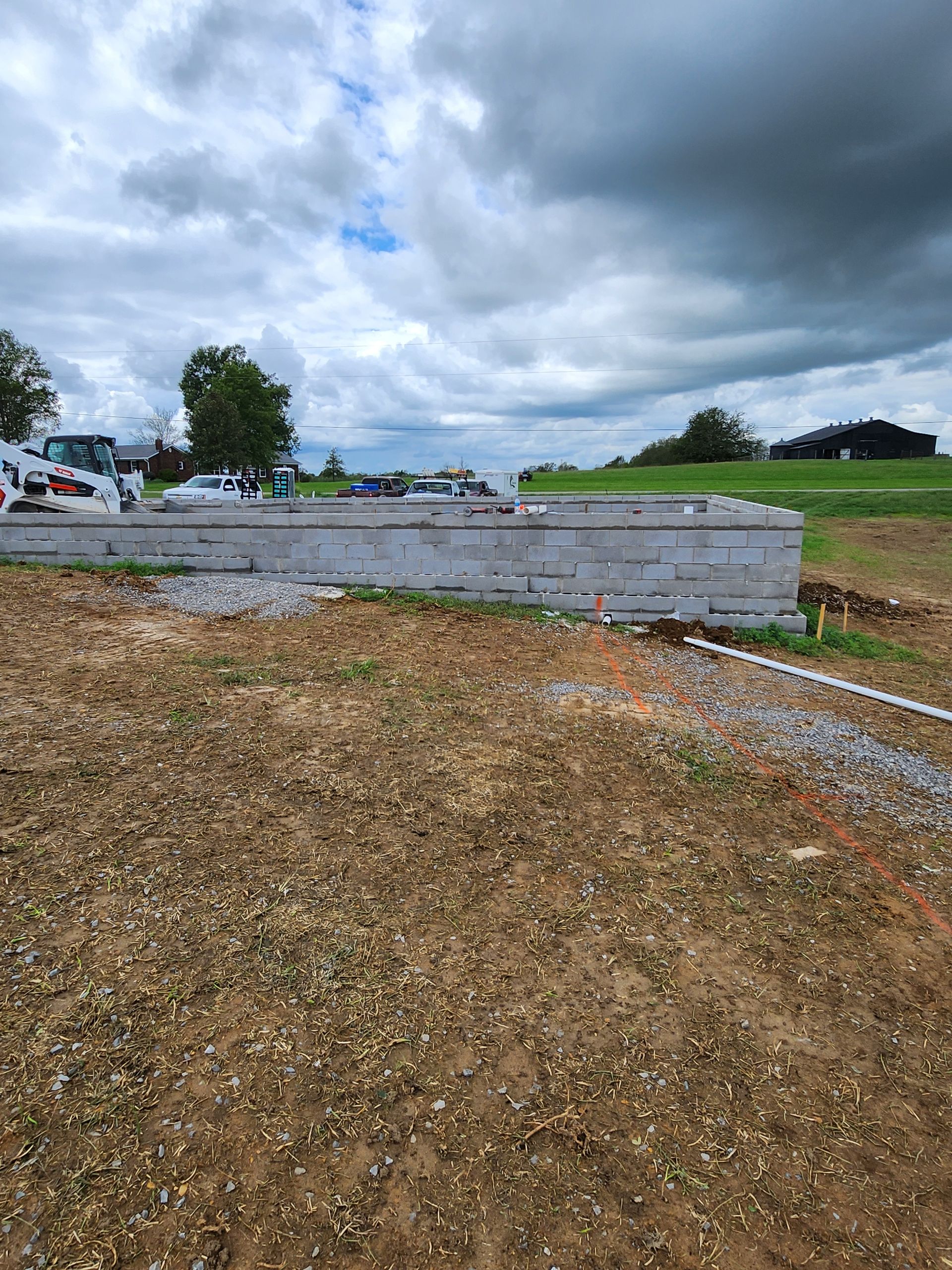 Open dirt lot beside a low concrete wall under a cloudy sky