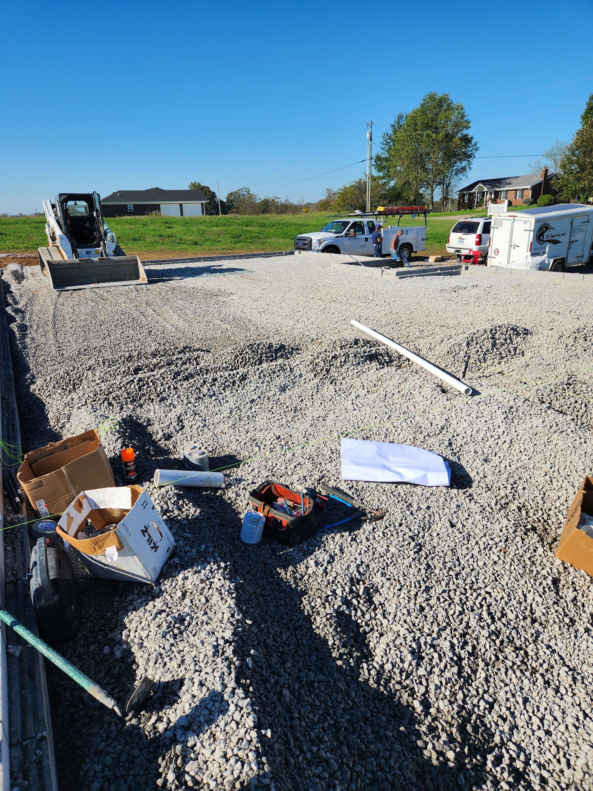 Construction site with gravel foundation, scattered materials, and vehicles under a clear blue sky