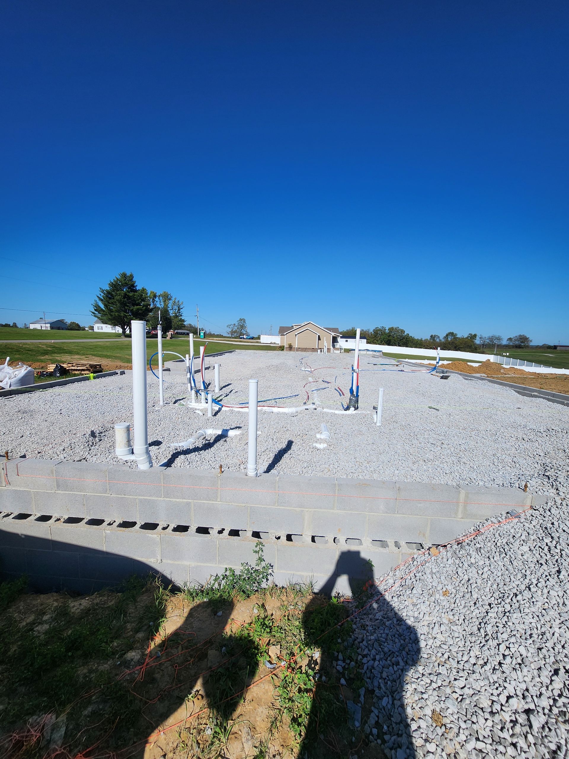 Gravel lot under construction with white posts, scattered pipes, and a clear blue sky