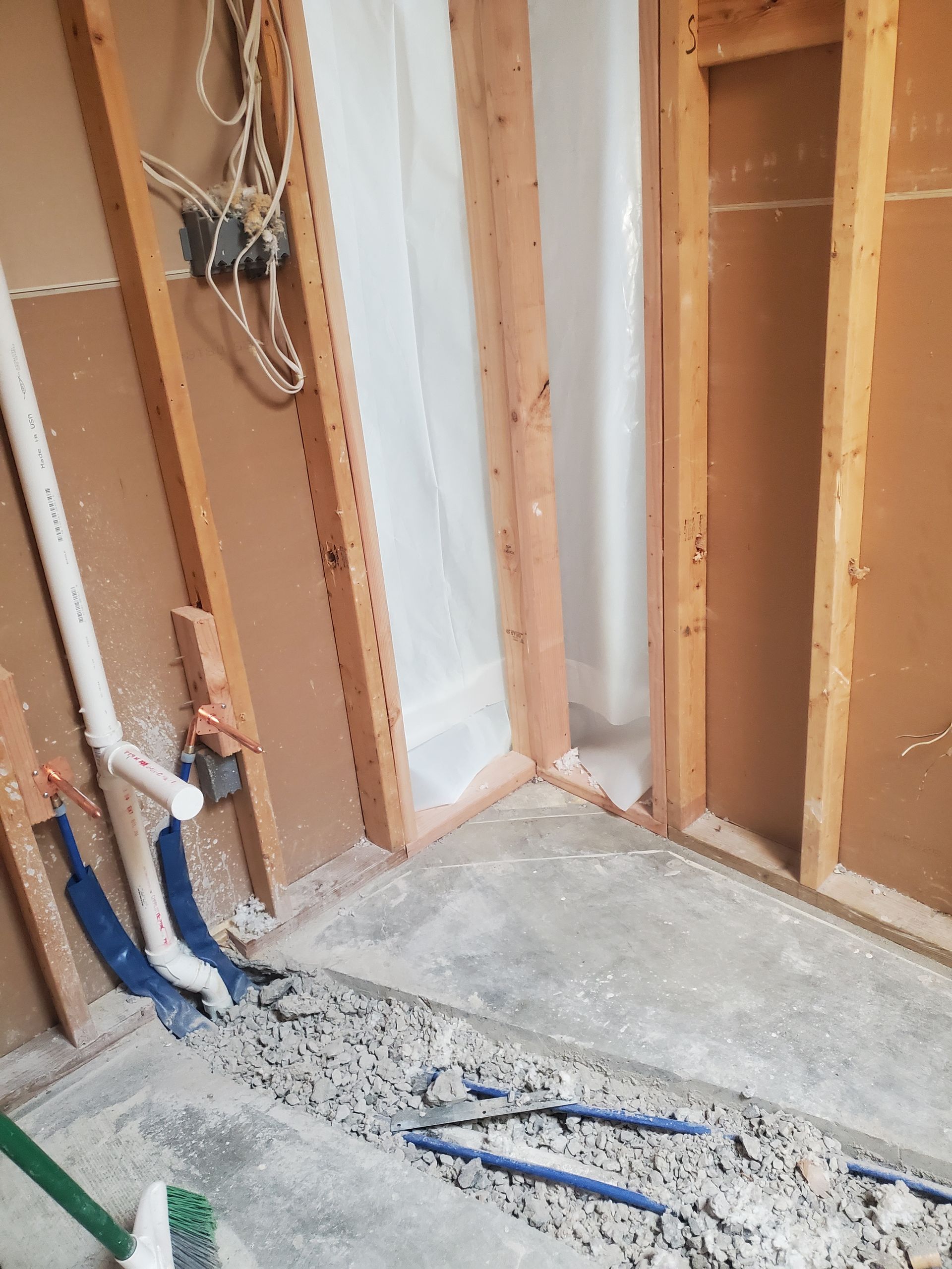 Exposed wall studs and plumbing in a partially renovated room with debris on the floor