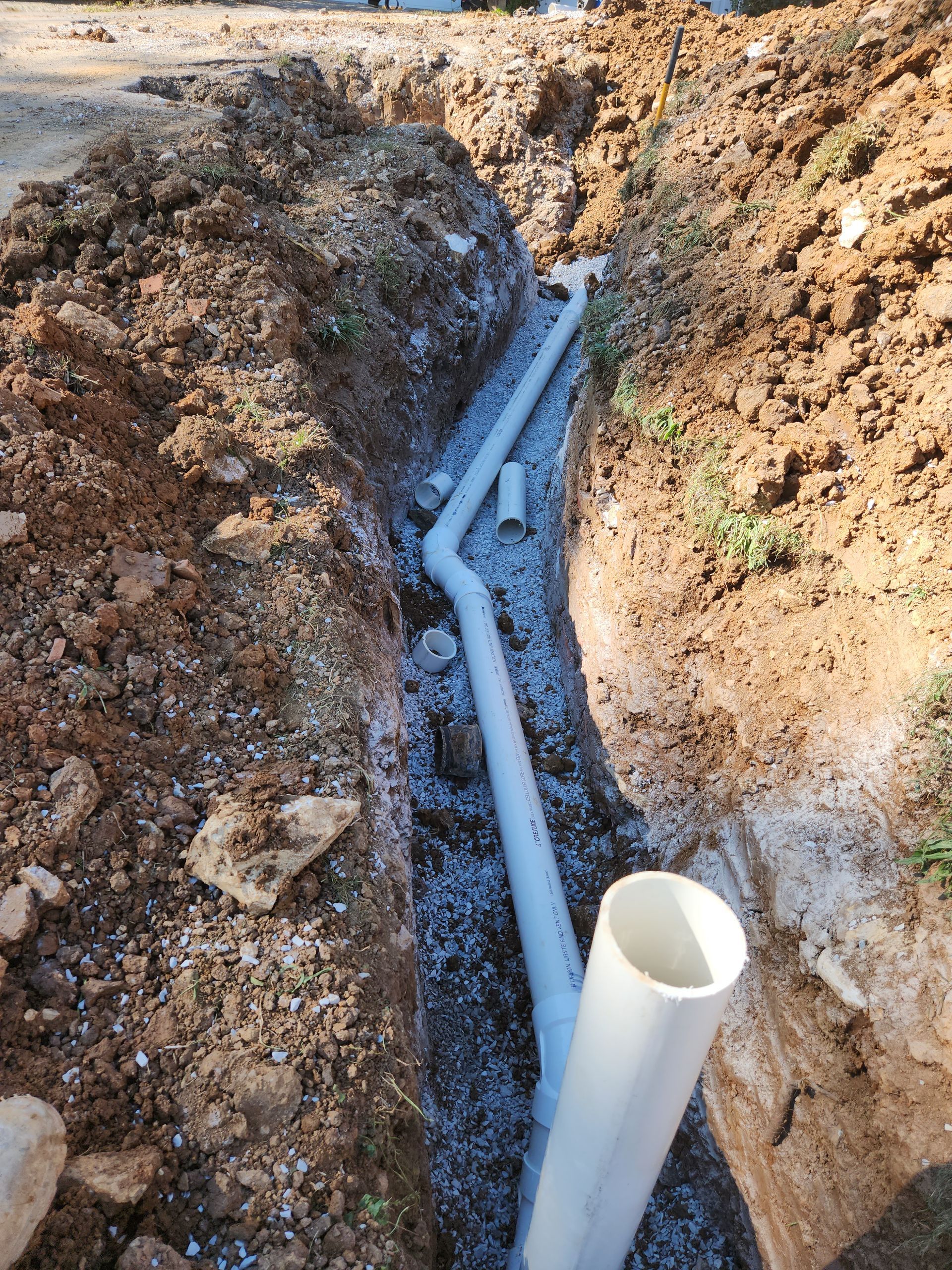 PVC pipes laid in a dirt trench beside an open white pipe
