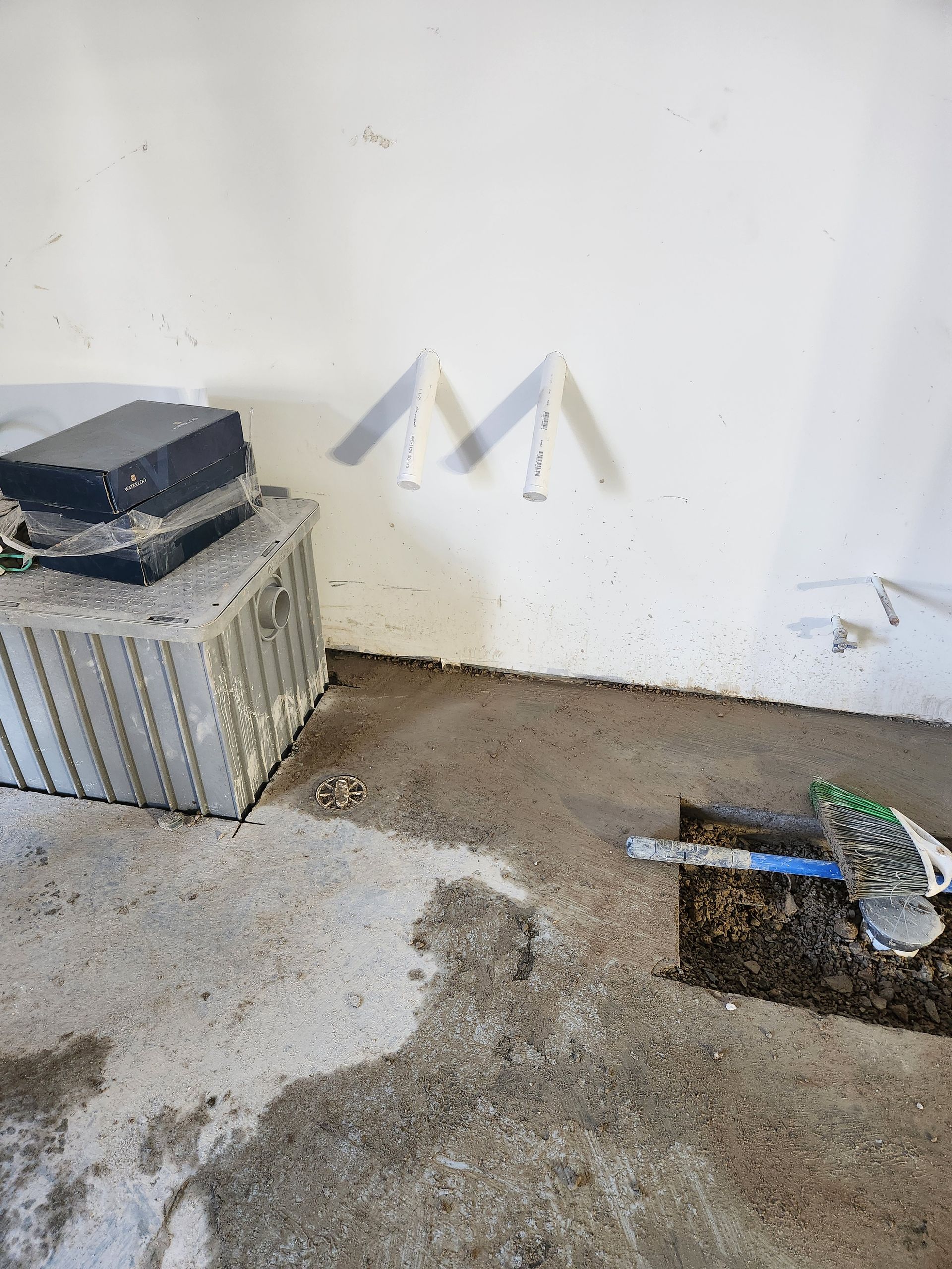 Dirty corner of a wall with debris, metal container on left, and an open drain or hole on the right
