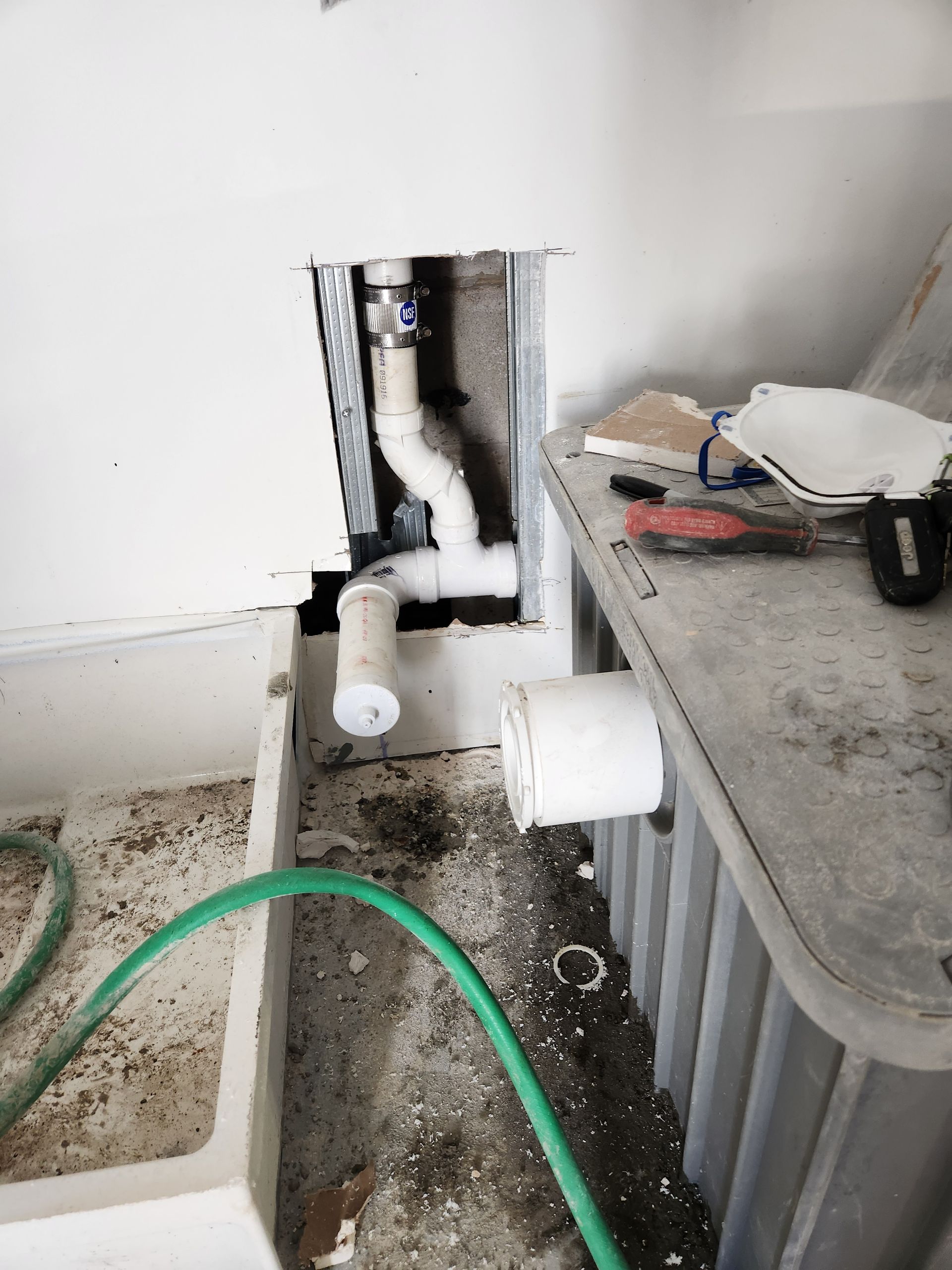 Exposed white plumbing pipes and a wall opening beside a gray utility sink in a messy room