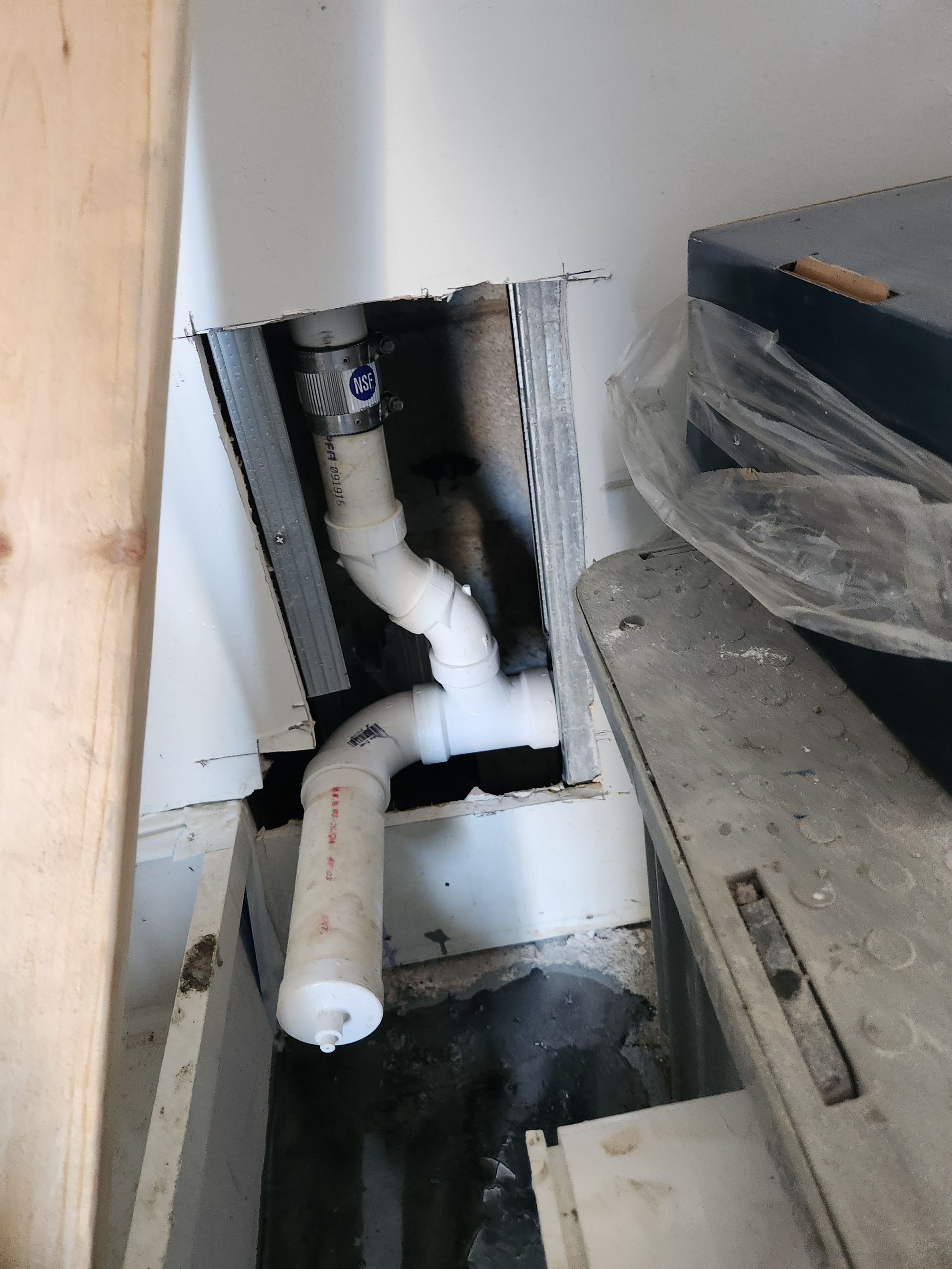 Exposed white PVC plumbing pipes inside a wall opening beside a concrete floor and cabinet.