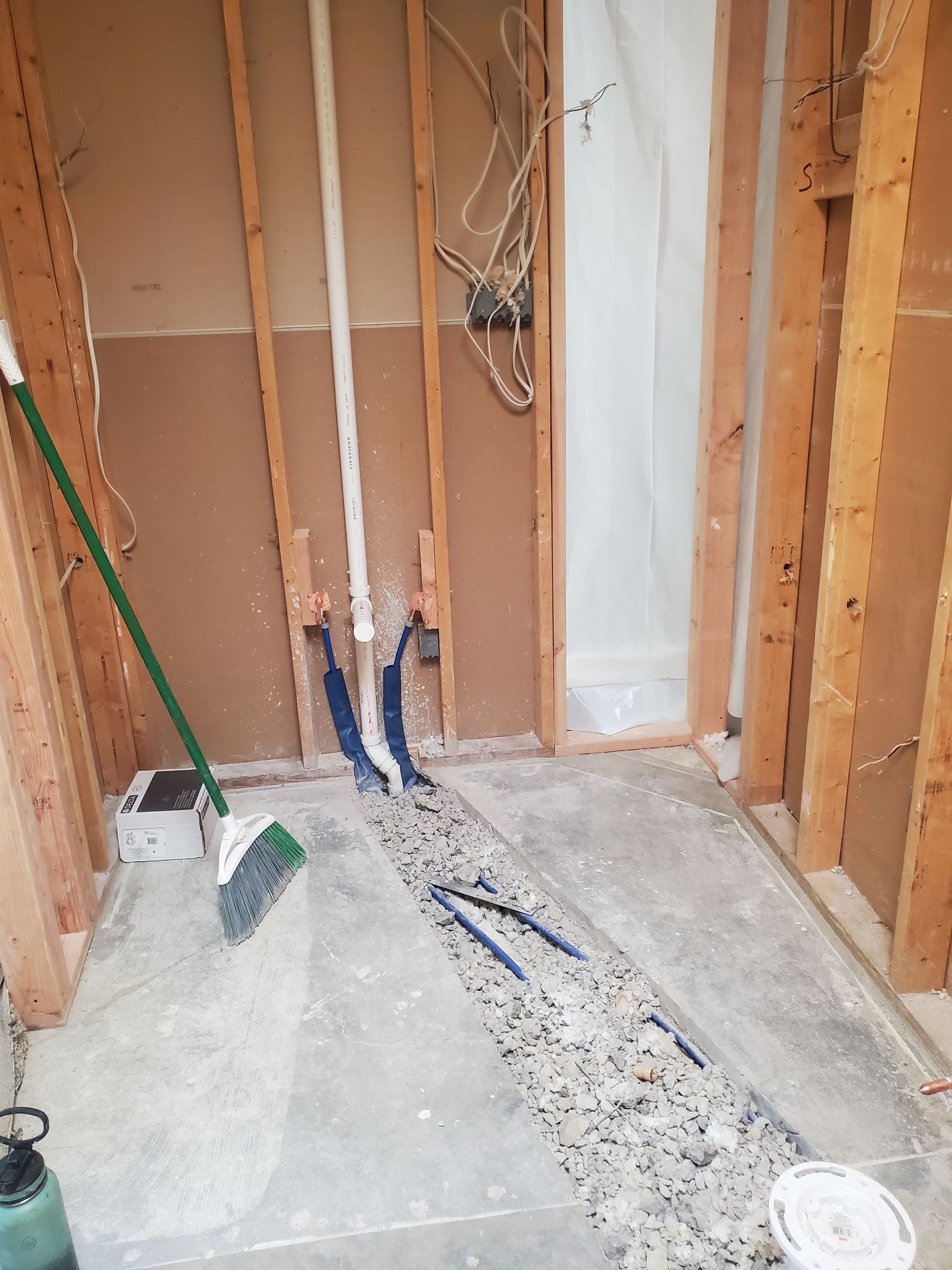 Partially renovated room with exposed wall studs, pipes, wires, and tools on a concrete floor.