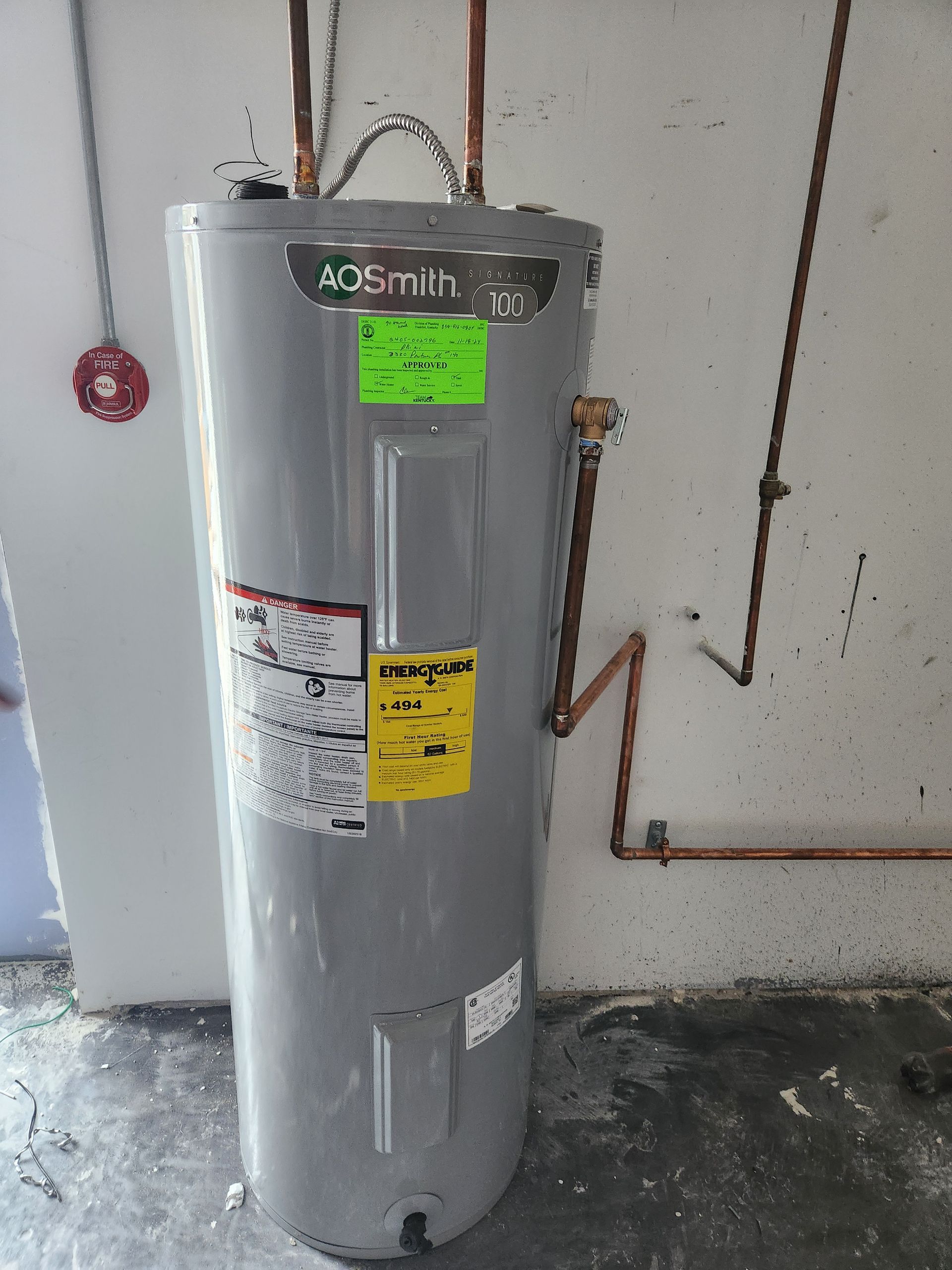 Tall gray water heater with labels and copper piping in a utility room