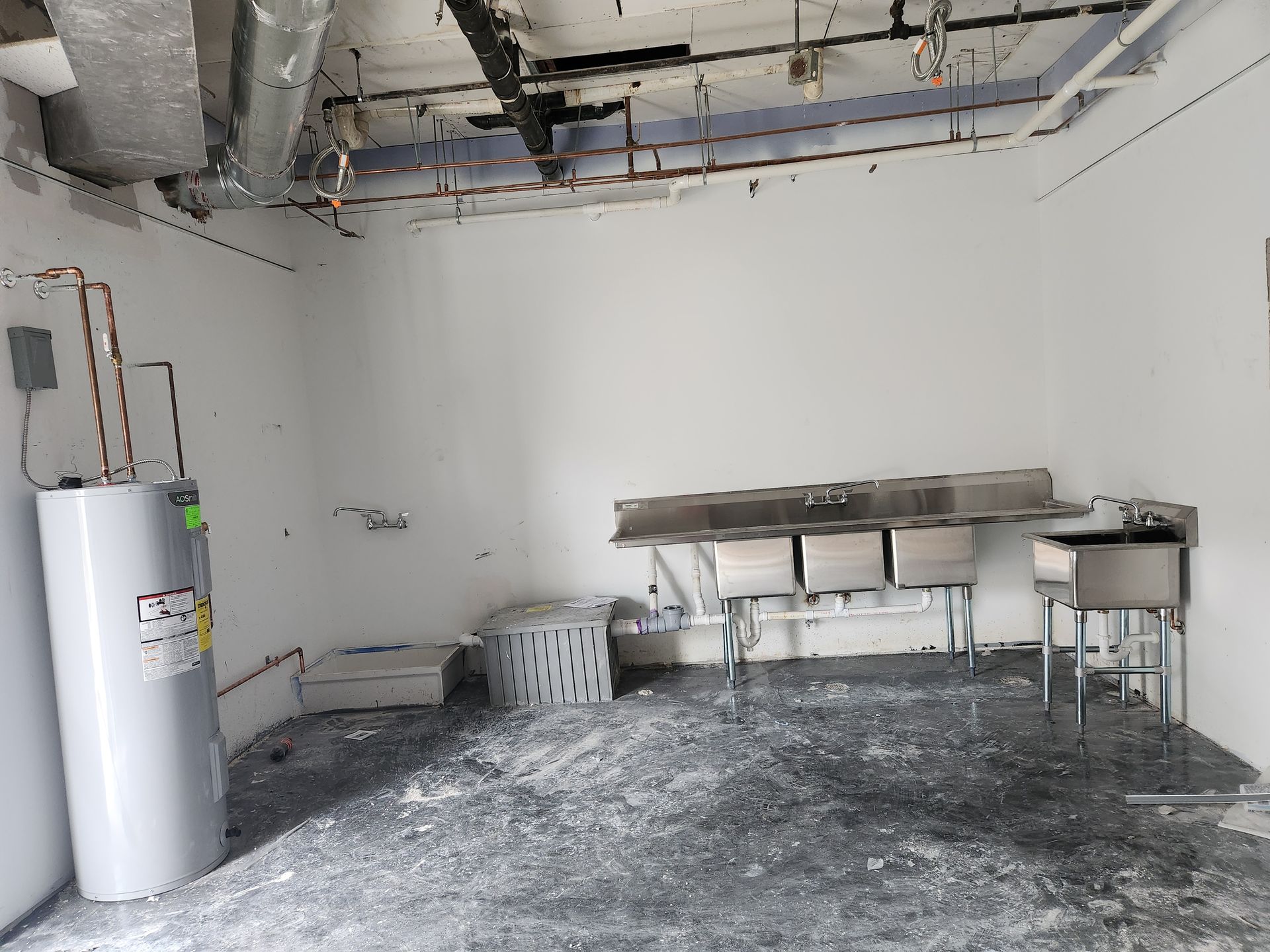 Empty unfinished room with exposed ceiling, water heater, sink, and construction debris on the floor.