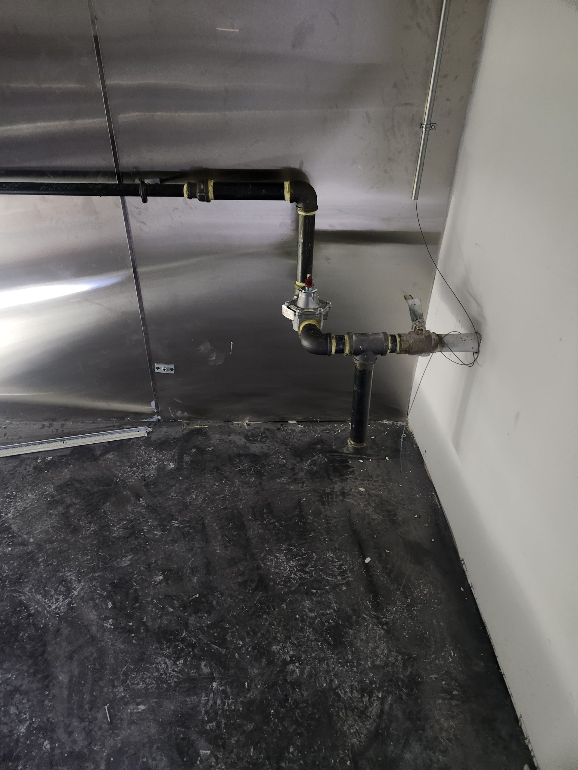 Metal pipes and a valve mounted on a wall, with a black floor below.