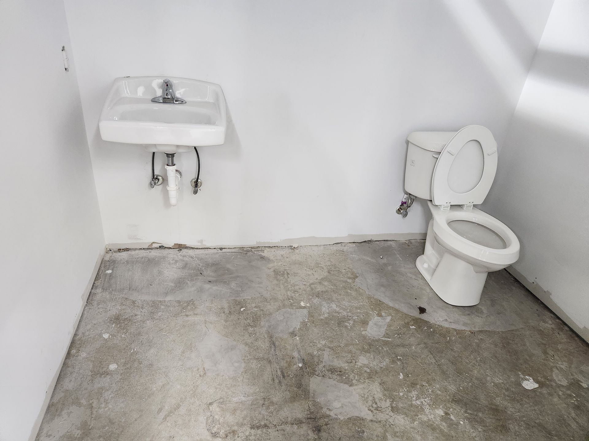 Empty unfinished bathroom with sink, toilet, and bare concrete floor