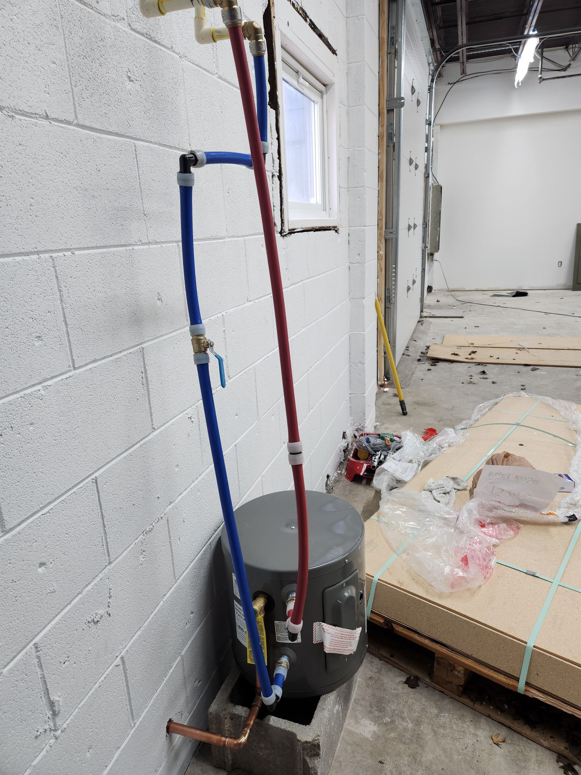 Utility pipes and a bucket beside a bed in a room under renovation