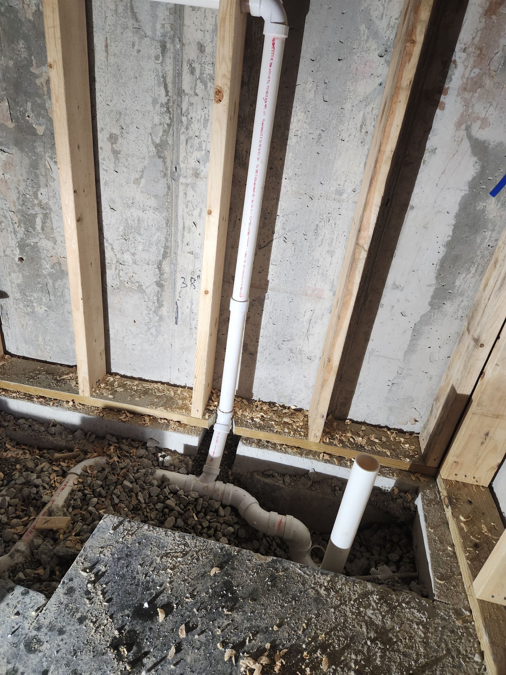 Exposed wall framing with pipes and rough concrete floor in a construction area