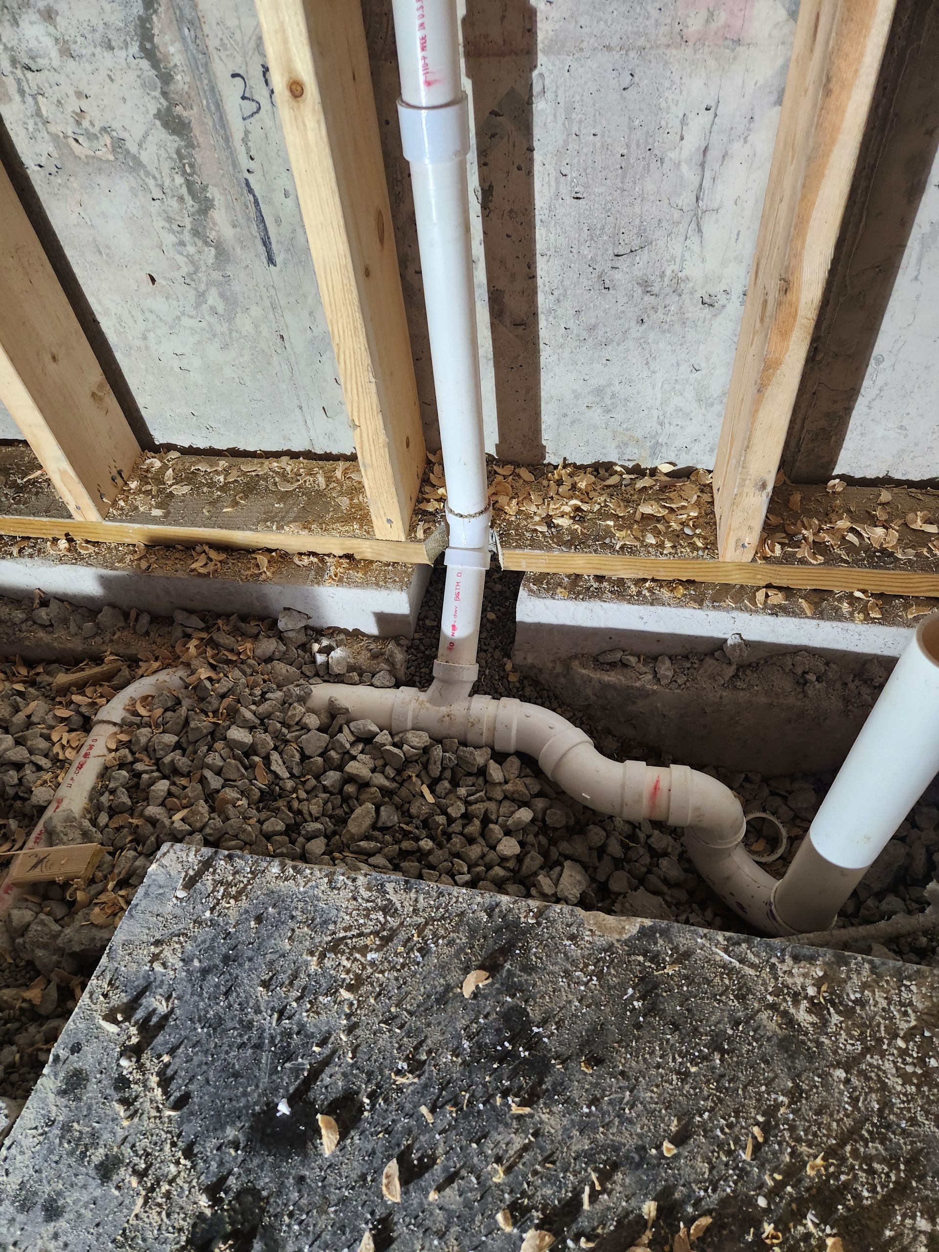 Exposed plumbing pipes in a wall cavity with gravel and concrete footing during construction