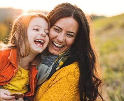A woman and a little girl are laughing together in a field.