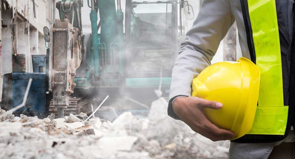 Operaio edile con indosso un elmetto giallo in un cantiere di demolizione polveroso.