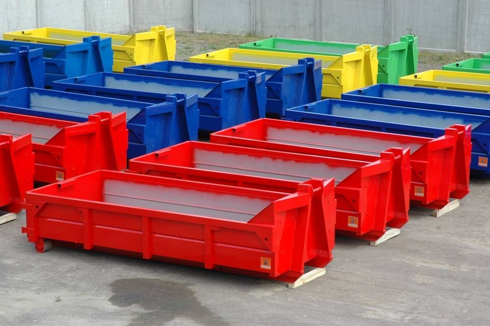 Colorati bidoni metallici industriali impilati all'aperto su un piazzale di cemento.