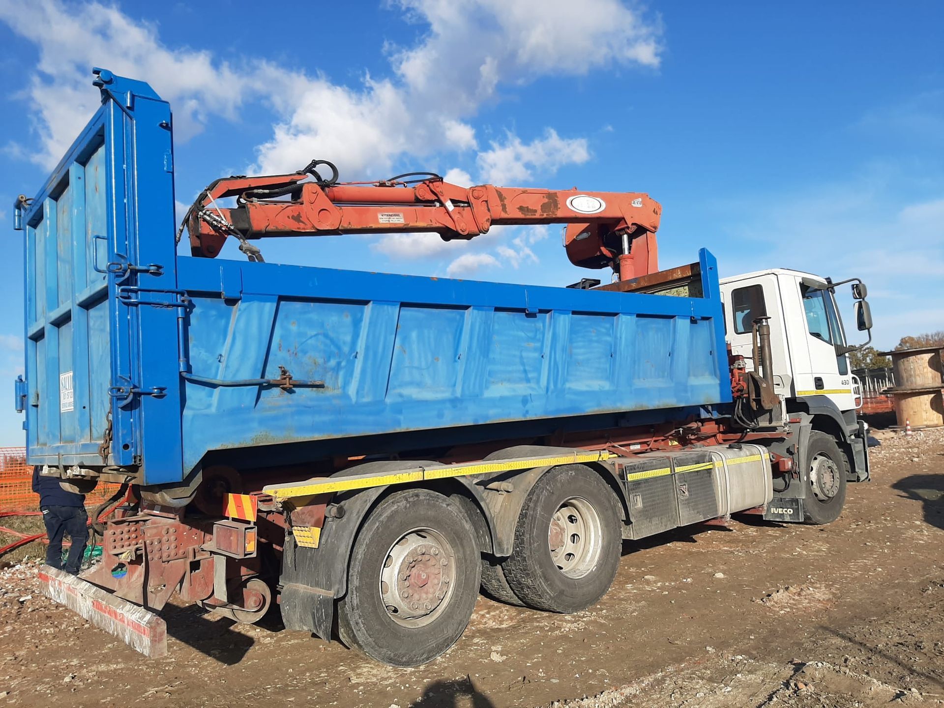 Un camion ribaltabile blu con una gru rossa carico di macerie in un cantiere.