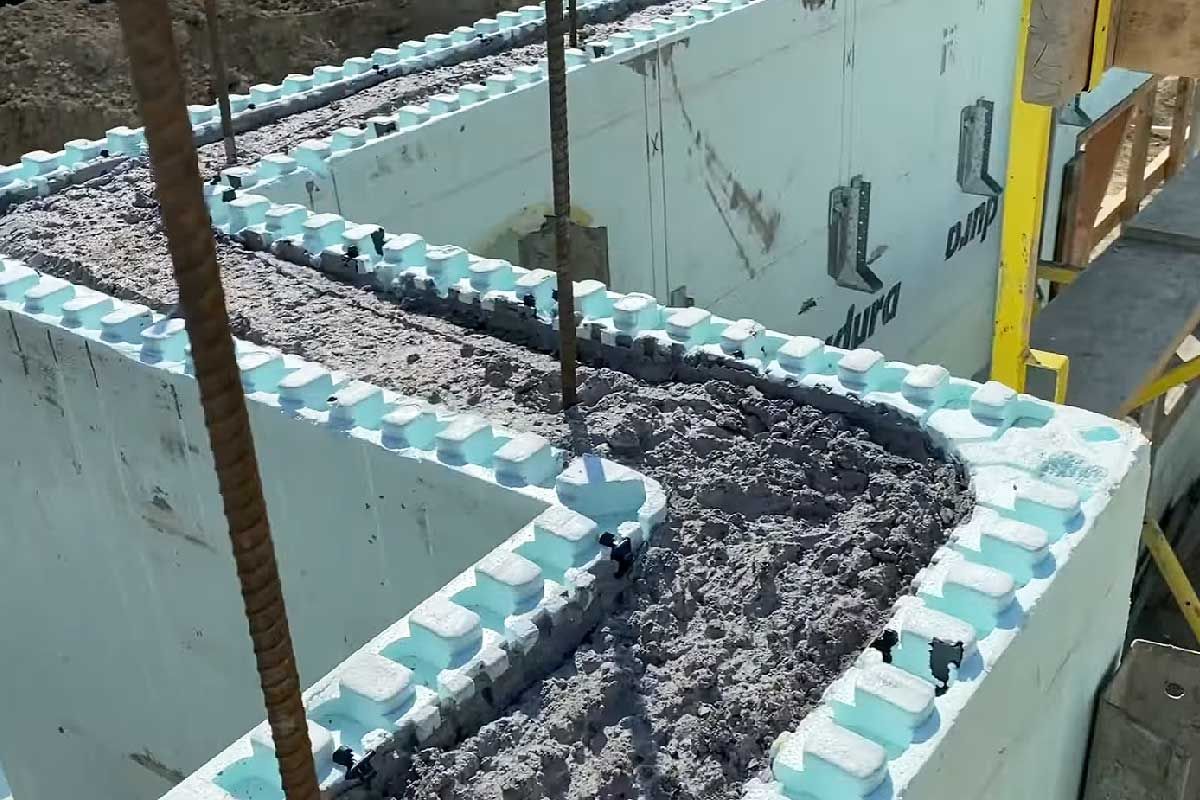 Construction d'un mur en béton courbe à l'aide de coffrages isolants (ICF). Des blocs de mousse bleue enrobent le béton.