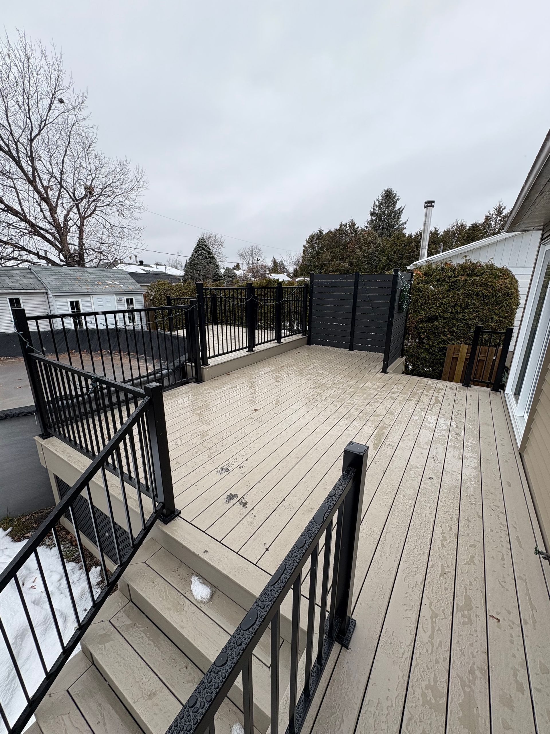 Terrasse avec rambardes noires, planches de bois et clôture pour préserver l'intimité, sous un ciel nuageux.
