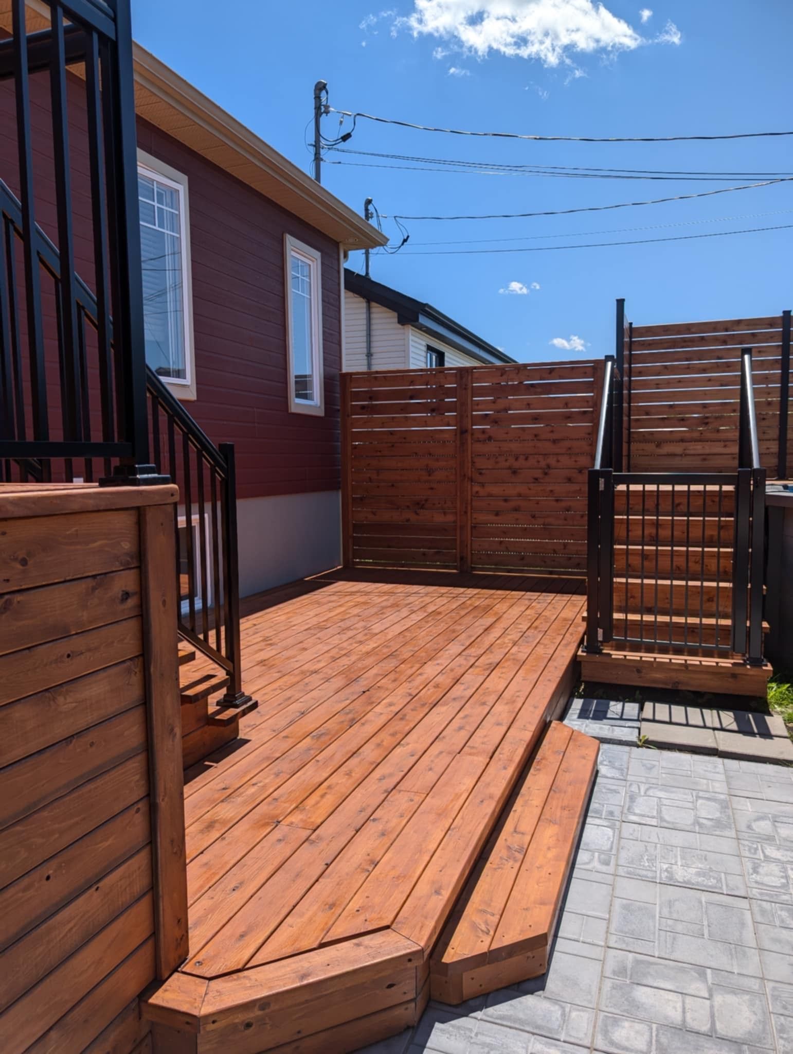 Terrasse en bois avec marches, clôture pour plus d'intimité et maison en arrière-plan par une journée ensoleillée.