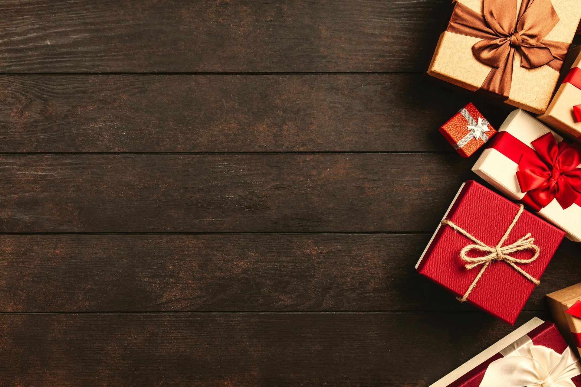 Gifts wrapped in various colors, tied with ribbons, arranged on a dark wooden surface.